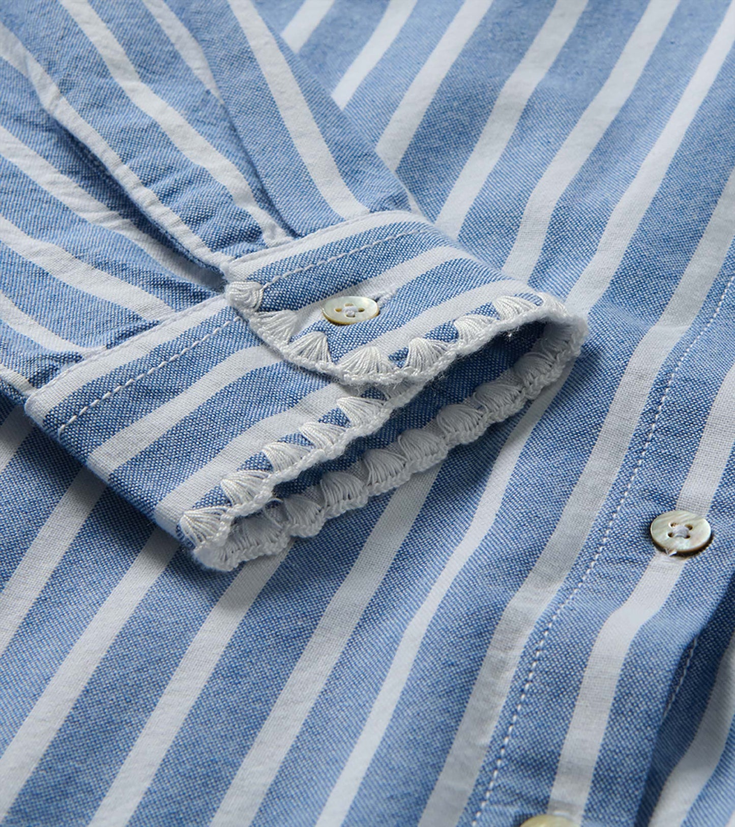 Close-up of blue and white striped cuff with button tab and white embroidered trim