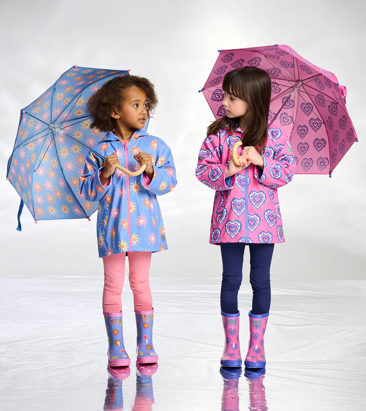 Girls wearing blue and pink heart-print rain boots with matching raincoats and umbrellas