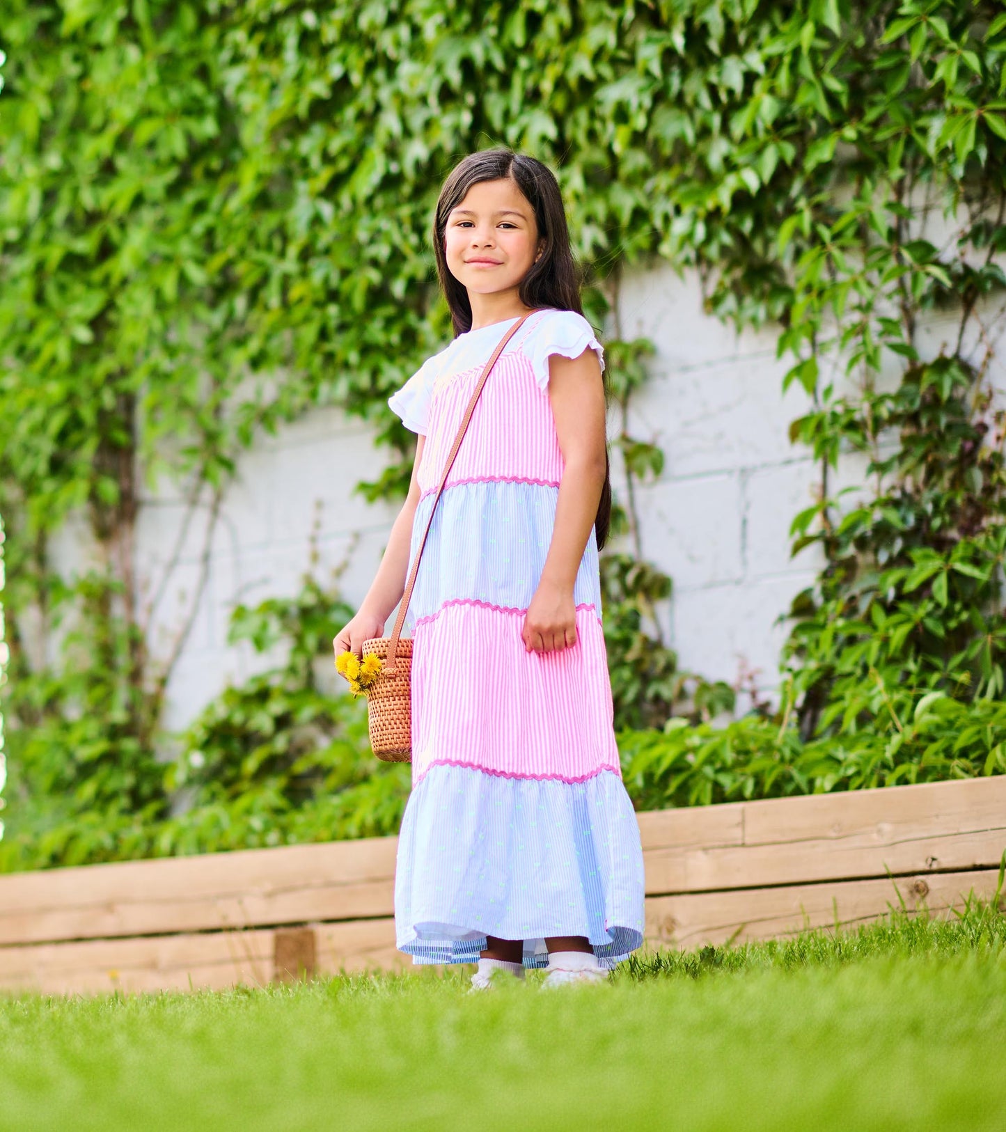 Side view of girls tiered midi dress with pink and blue striped panels and pink scalloped trim