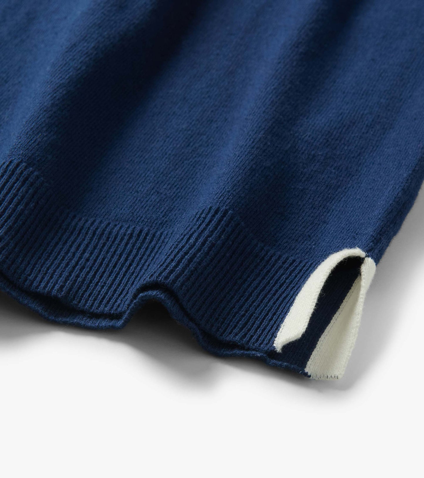 Close-up of a navy blue knit top hem with ribbed trim and a white sleeve cuff detail.