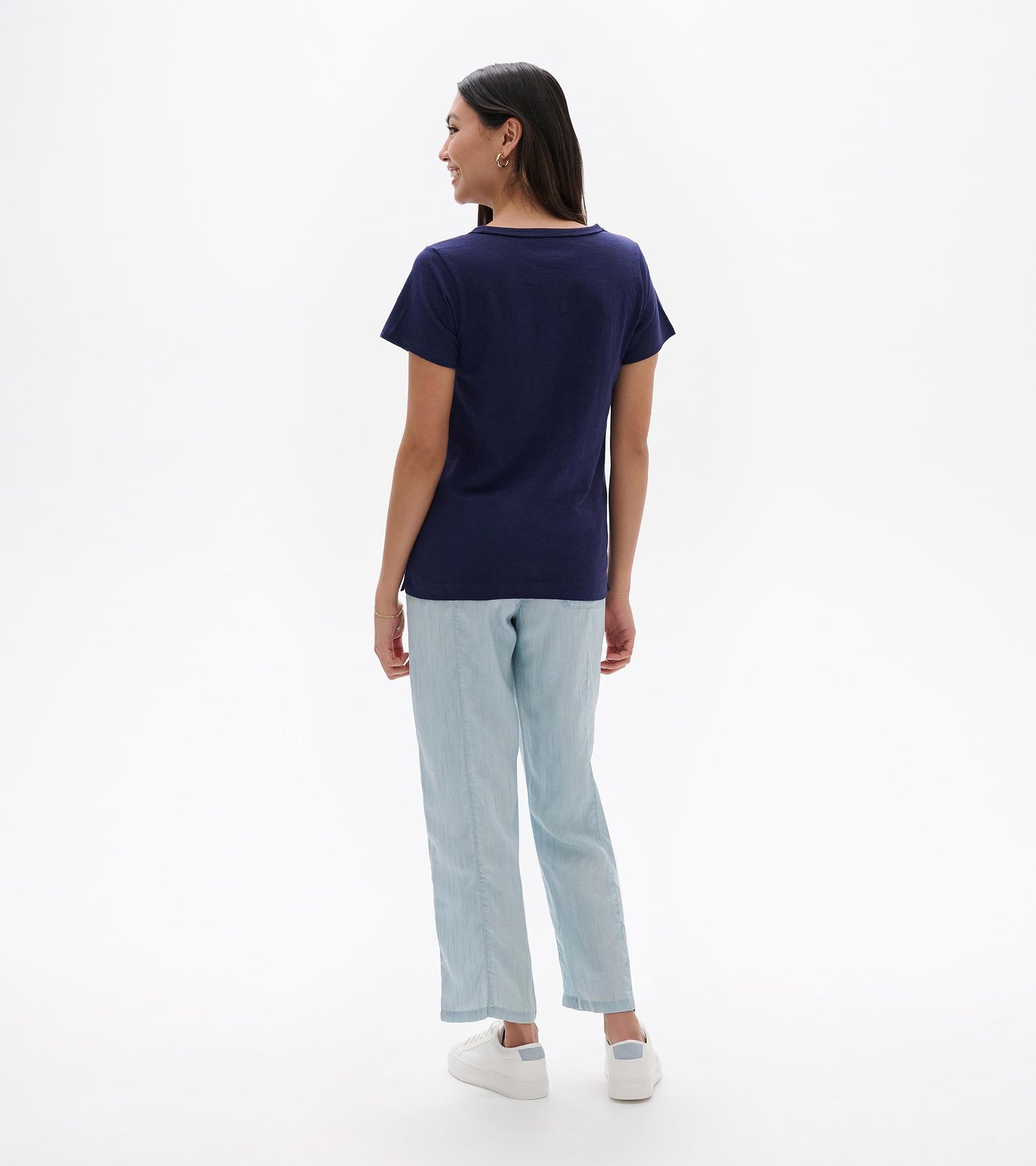 Back view of a navy short-sleeve crew neck tee on a model, paired with light blue pants.