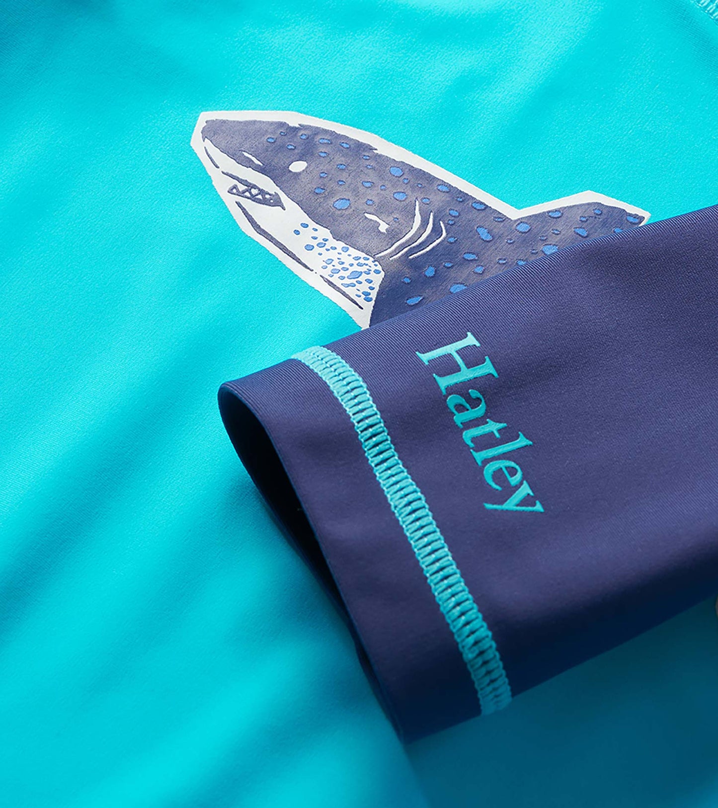 Turquoise boys rashguard with shark graphic and navy sleeve cuff detail