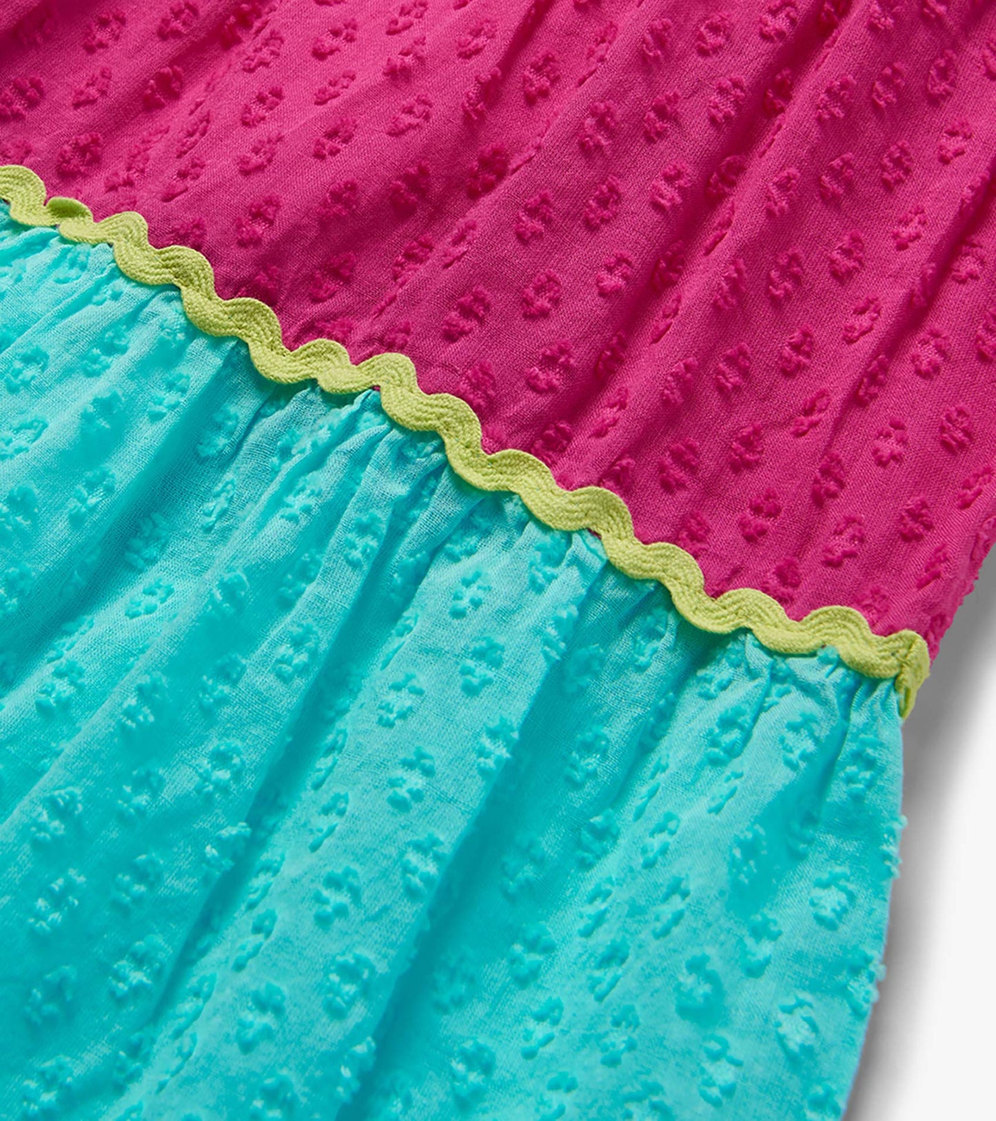 Close-up of a girls' midi dress with pink and turquoise color blocks and lime scalloped trim, textured fabric