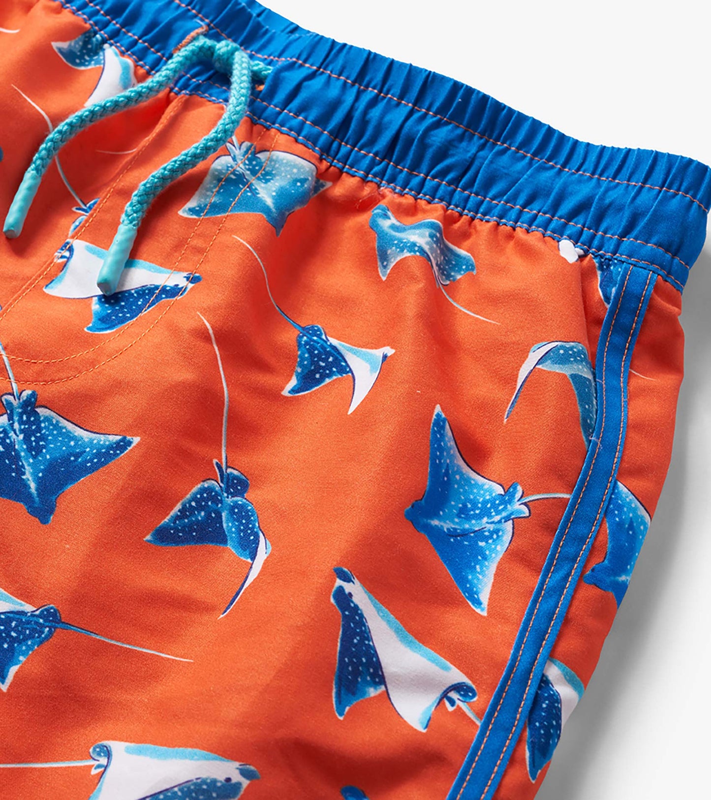 Orange boys swim trunks with blue stingray print, blue waistband, and turquoise drawstring close-up