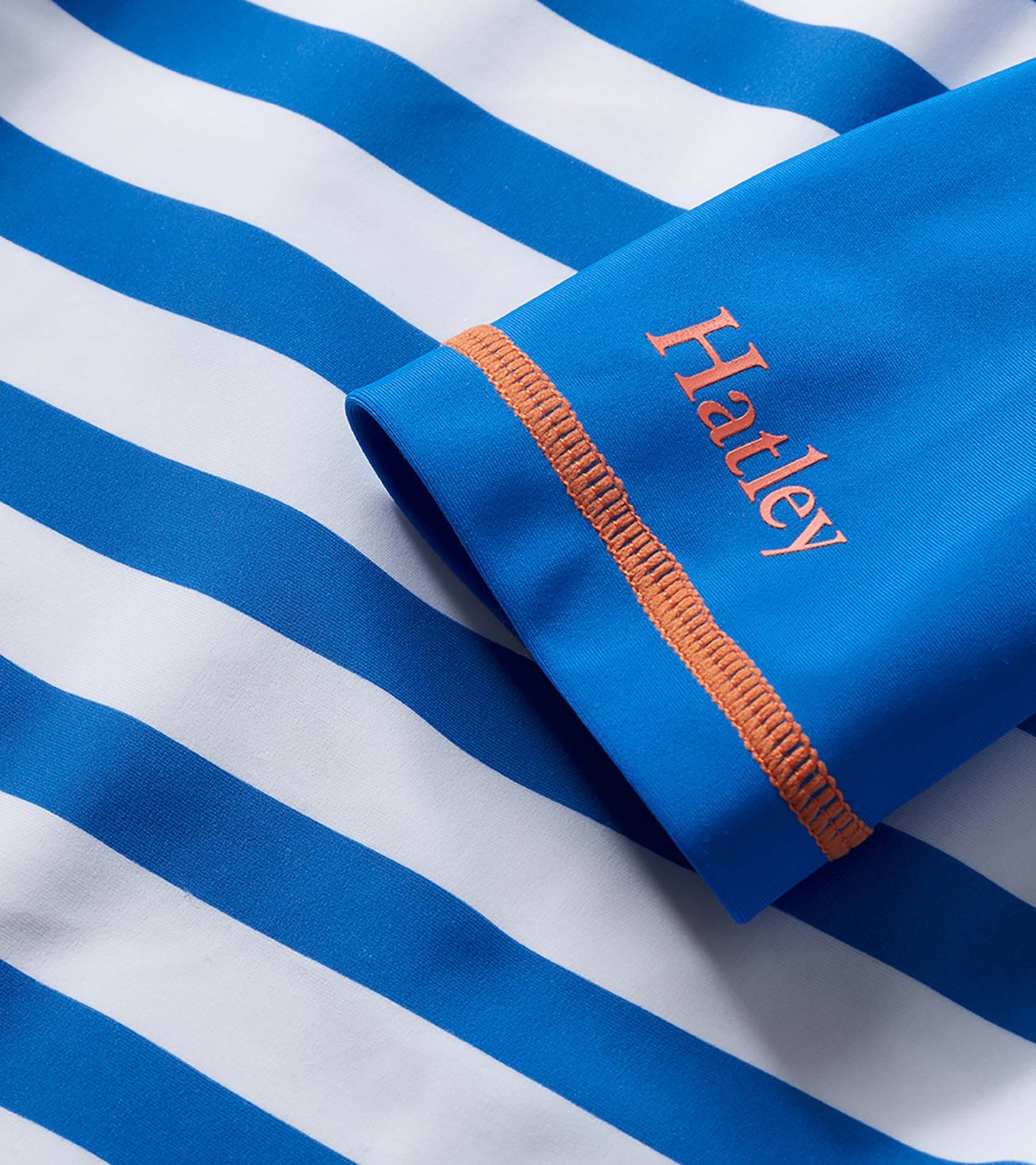 Blue and white striped boys' rashguard with orange stitching and sleeve cuff detail, close-up view