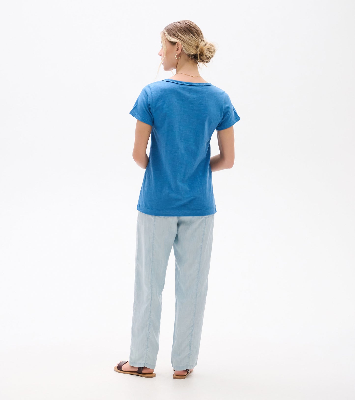 Back view of a blue short-sleeve crew neck tee on a model, paired with light pants.