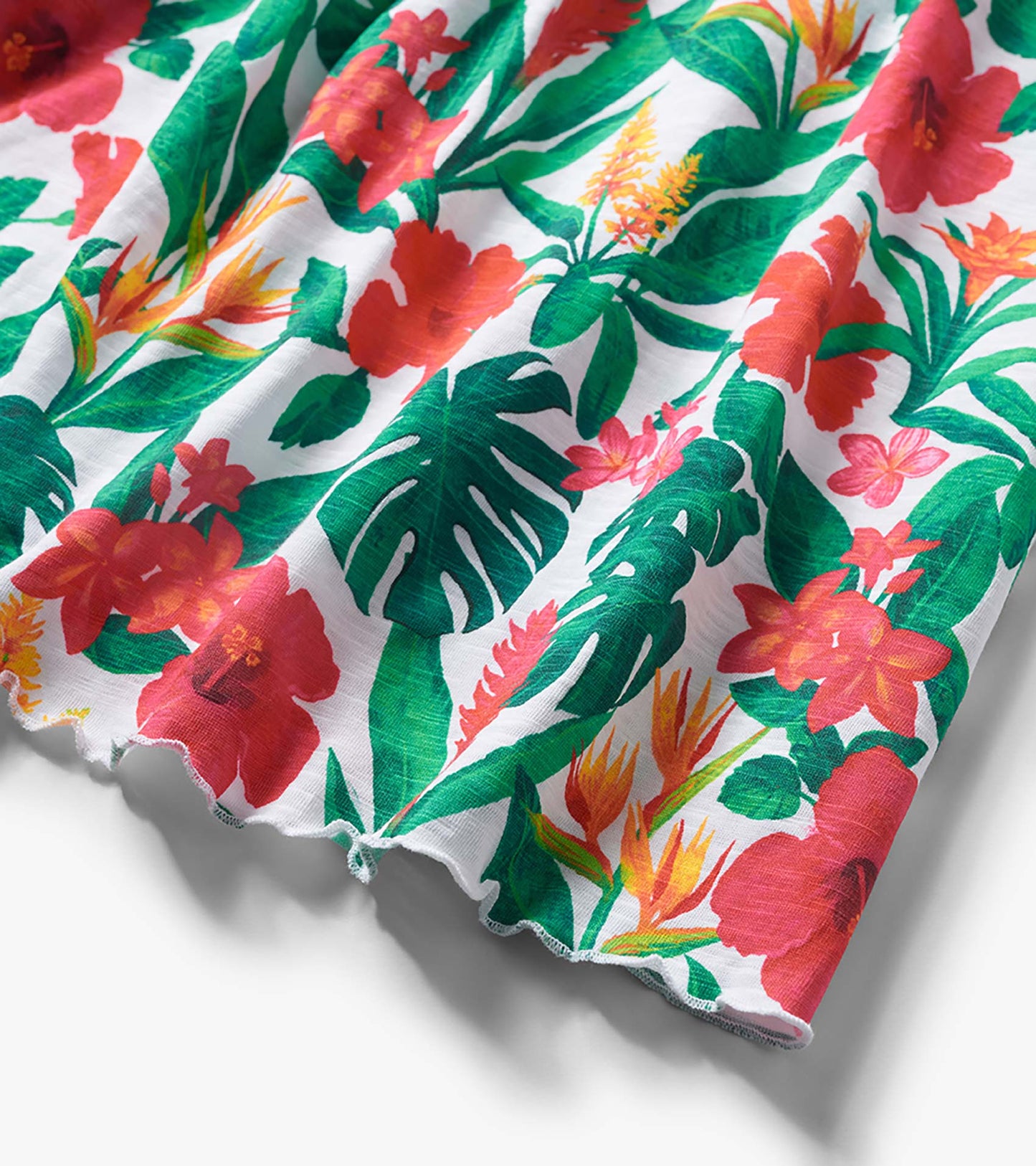 White dress fabric with green leaves and pink-red tropical flowers, close-up of hemline