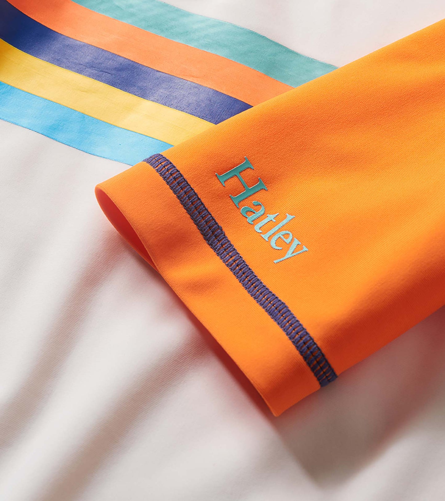 Orange boys’ short sleeve rashguard with blue stitching and multicolor striped sleeves, folded close-up