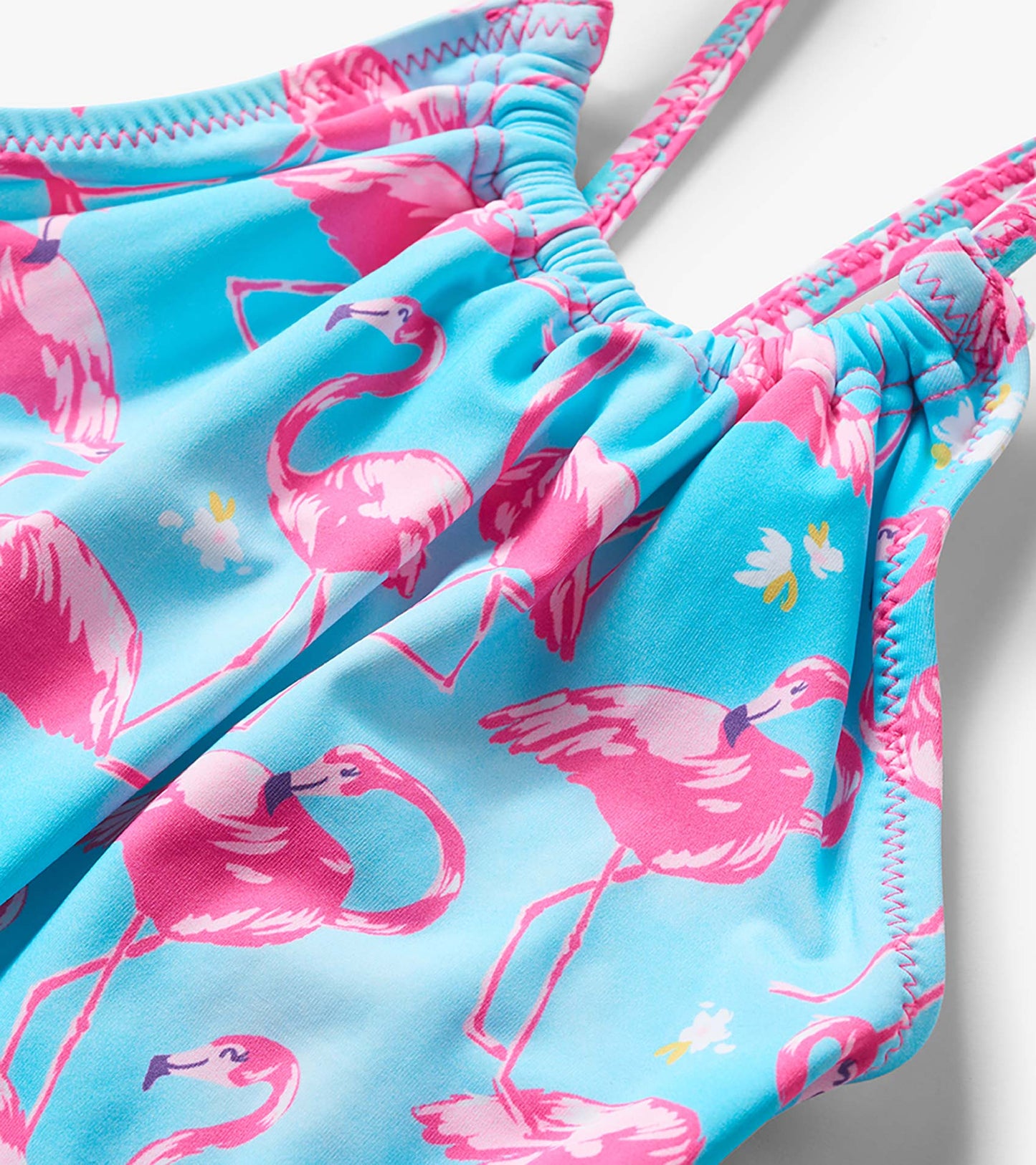 Close-up of a blue girls' one-piece swimsuit with pink flamingo print and pink zigzag trim straps