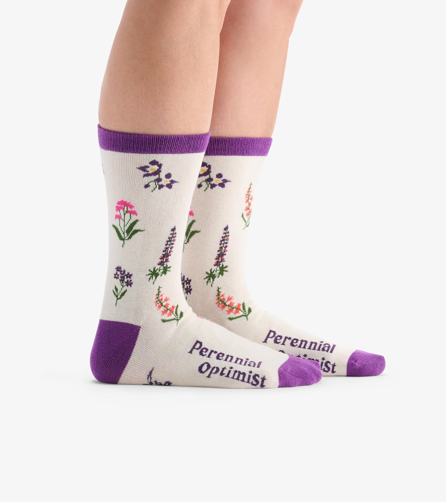 Cream crew socks featuring colorful wildflower patterns and purple accents, with "Perennial Optimist" text on the toes.