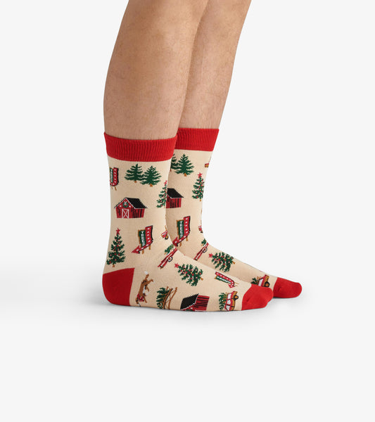 Beige crew socks featuring a Christmas tree farm pattern with red accents, including cabins, trees, and sleds.