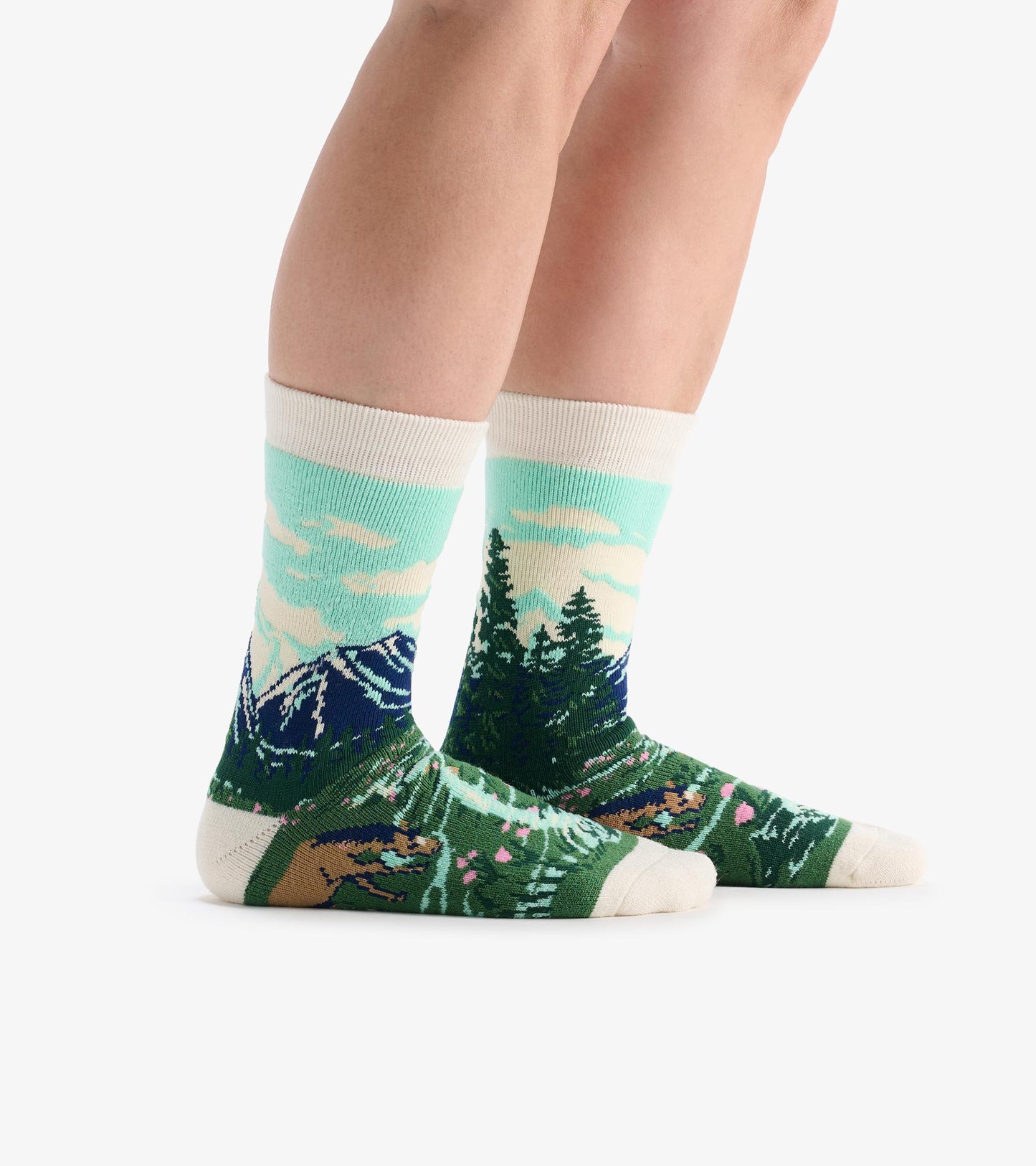 Crew socks with mountain and forest landscape pattern in teal, green, navy, and cream, shown on legs.