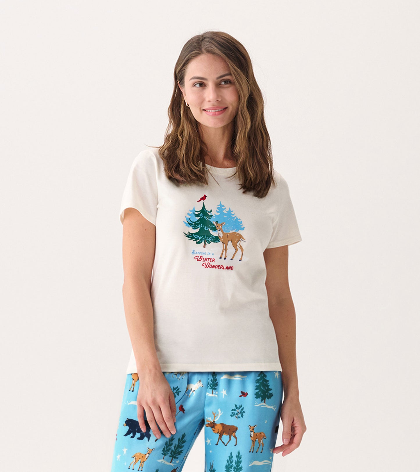 Cream short-sleeve pajama t-shirt featuring a winter scene with trees and a deer, worn with blue patterned pajama pants.