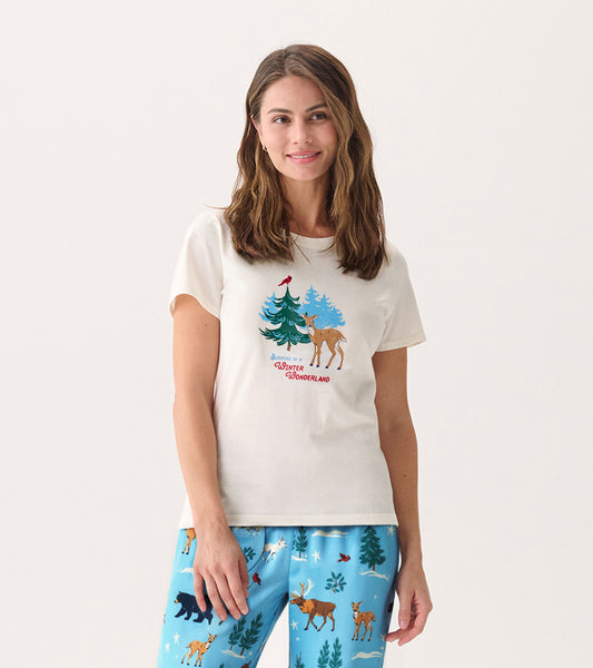 Cream short-sleeve pajama t-shirt featuring a winter scene with trees and a deer, worn with blue patterned pajama pants.