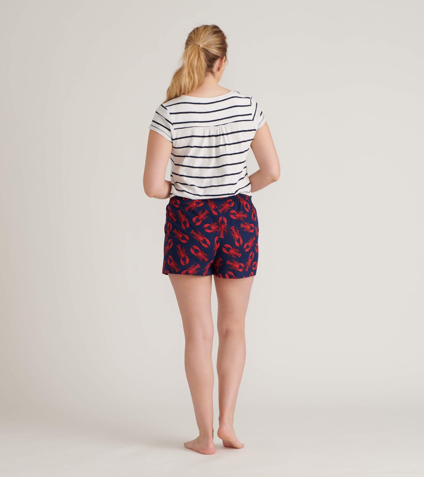 Women's striped V-neck tee in white and navy, featuring a relaxed fit and short sleeves, worn with patterned shorts.