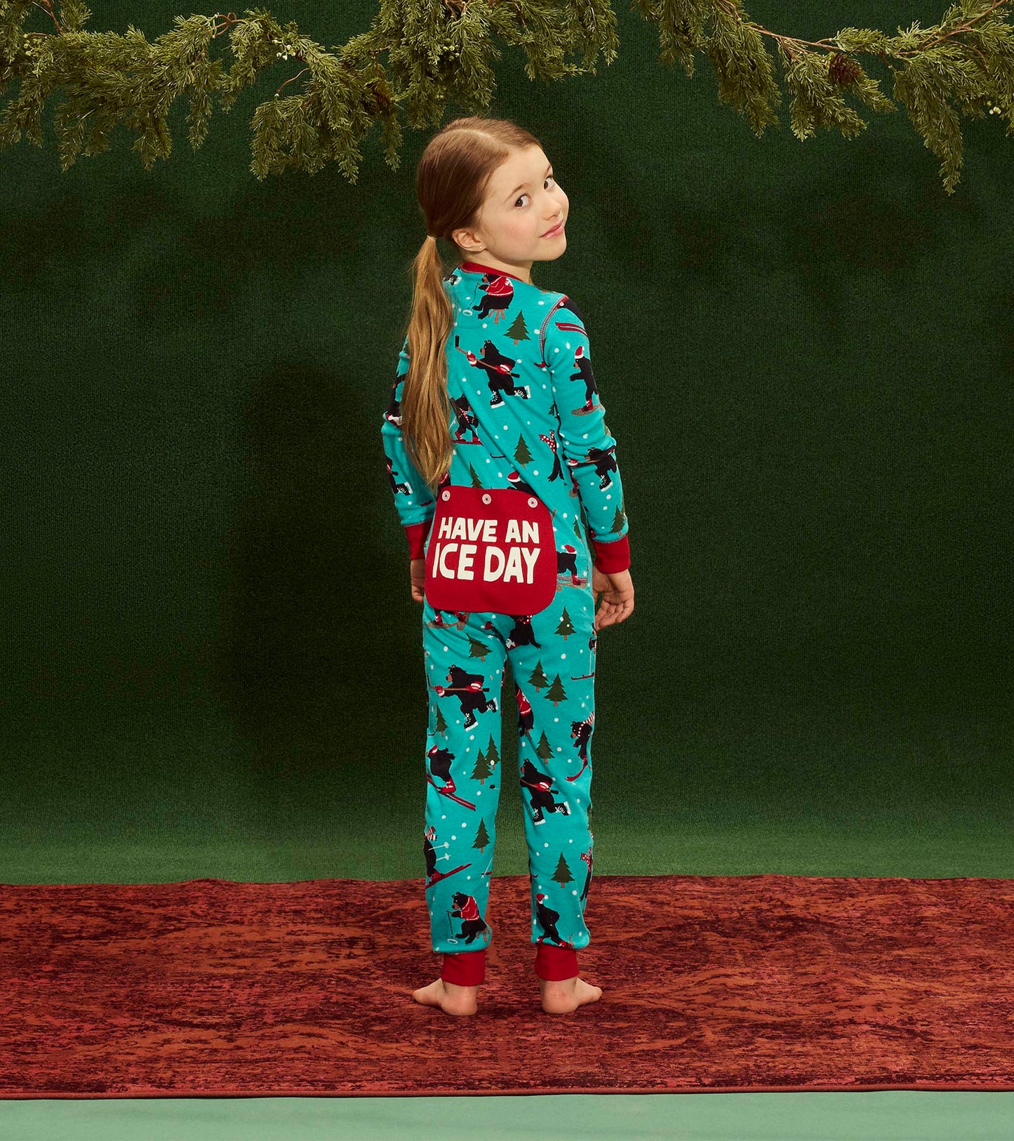 Turquoise kids' onesie with festive patterns, red cuffs, and a "Have an Ice Day" pocket, shown from the back.