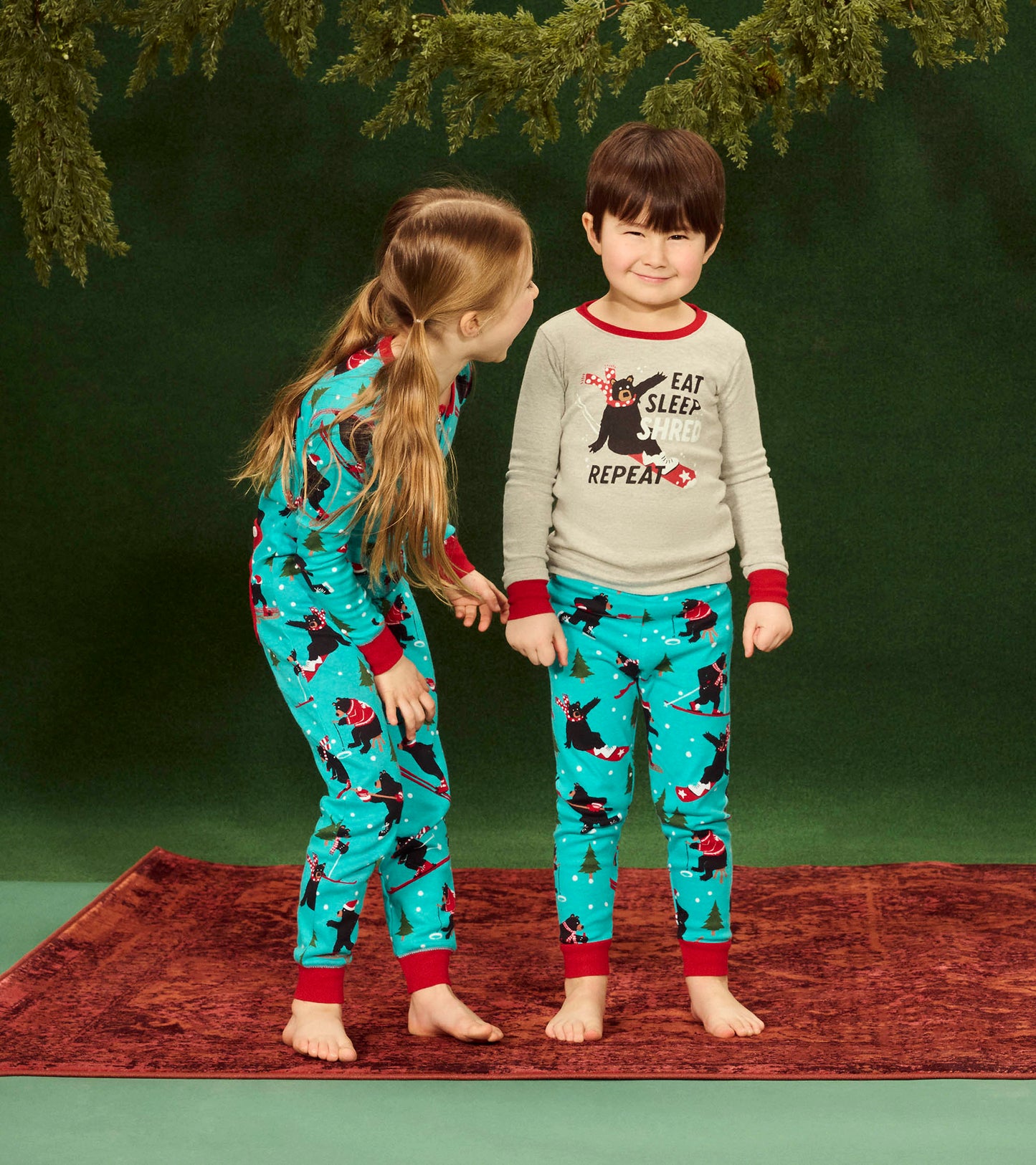 Turquoise kids' onesie with festive bear print, red cuffs, and a long-sleeve top featuring a playful slogan.