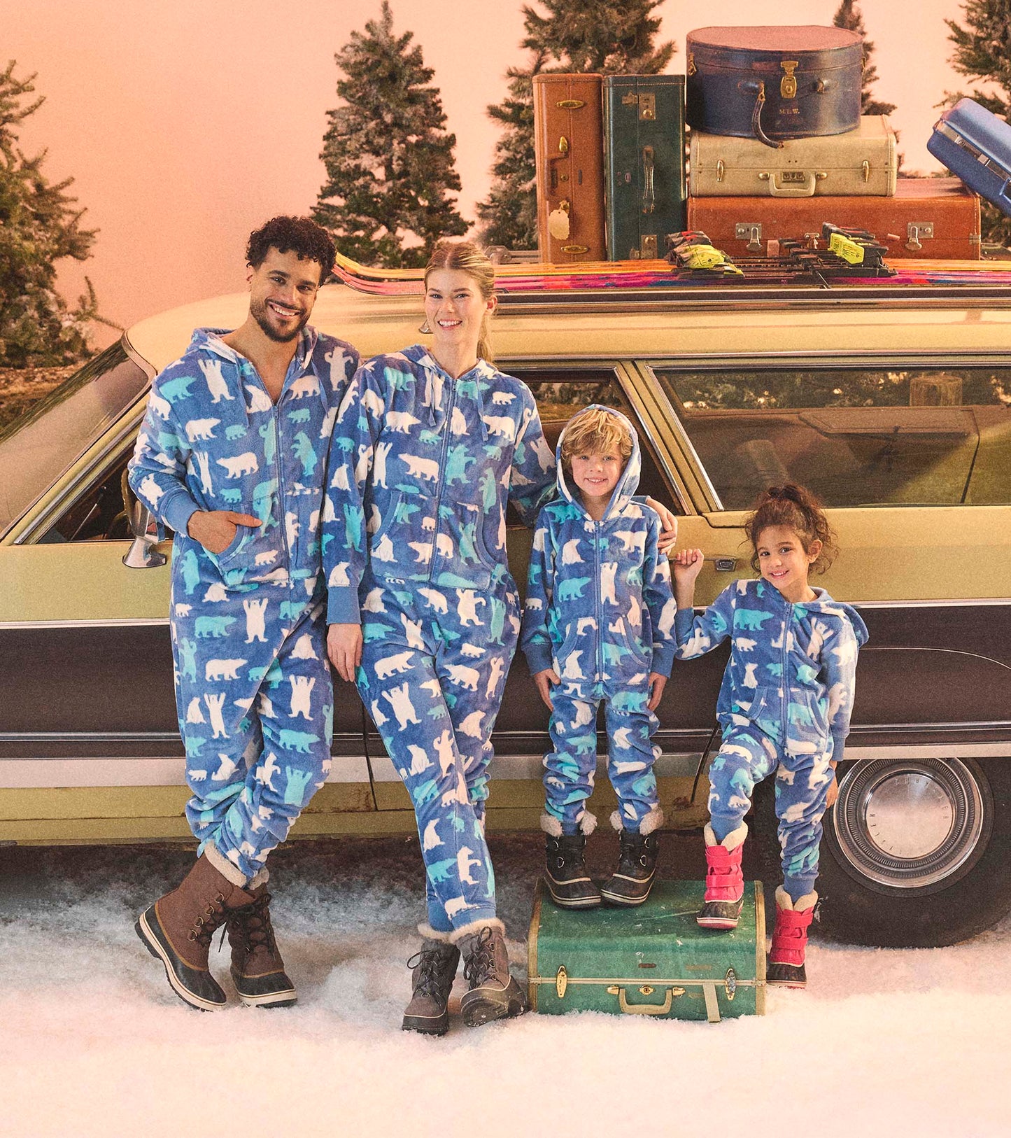 Blue fleece jumpsuits with polar bear patterns, worn by adults and children, set against a snowy backdrop and vintage car.