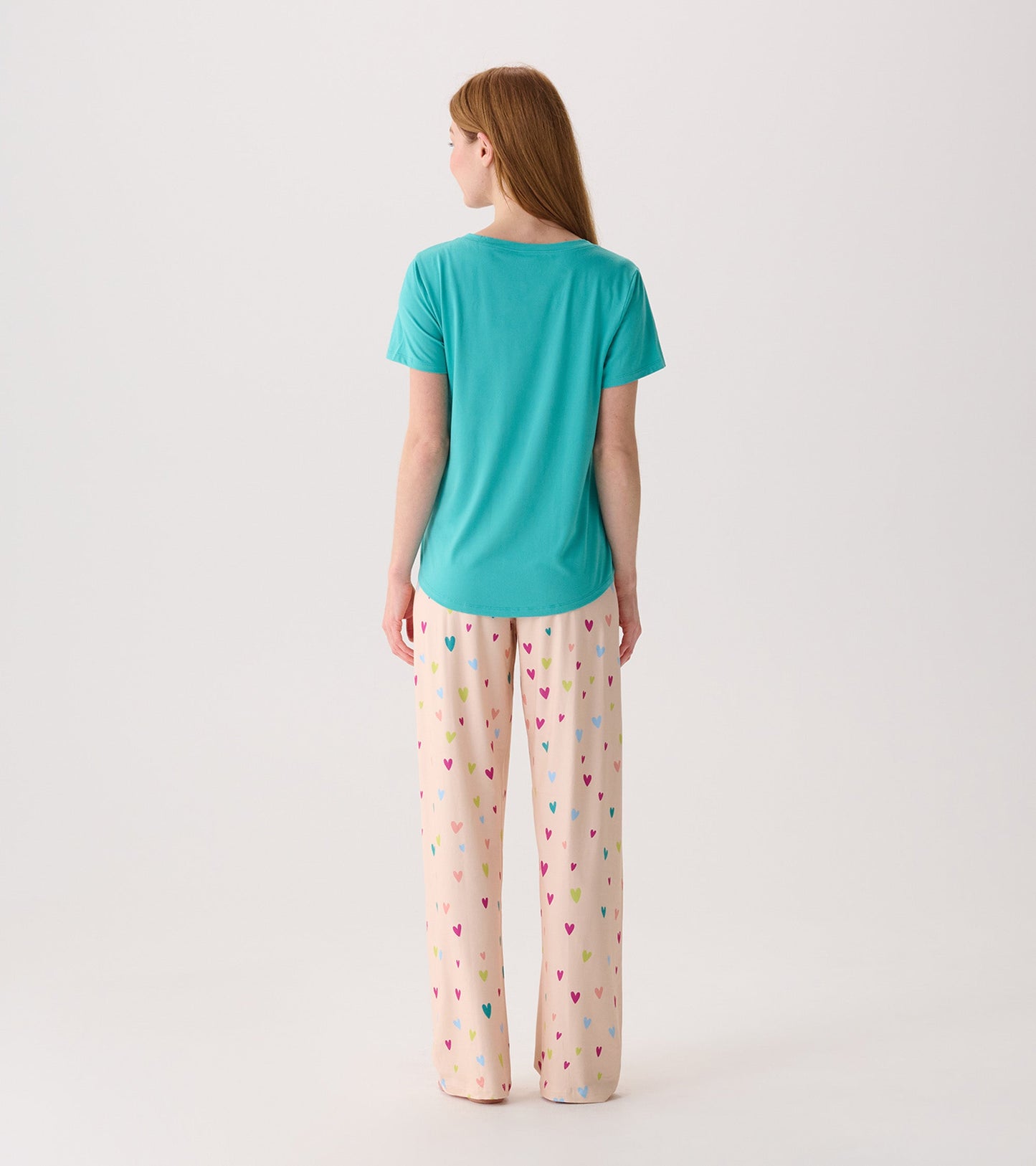 Turquoise V-neck T-shirt made from soft polyknit, worn with patterned heart-print pants, viewed from the back.