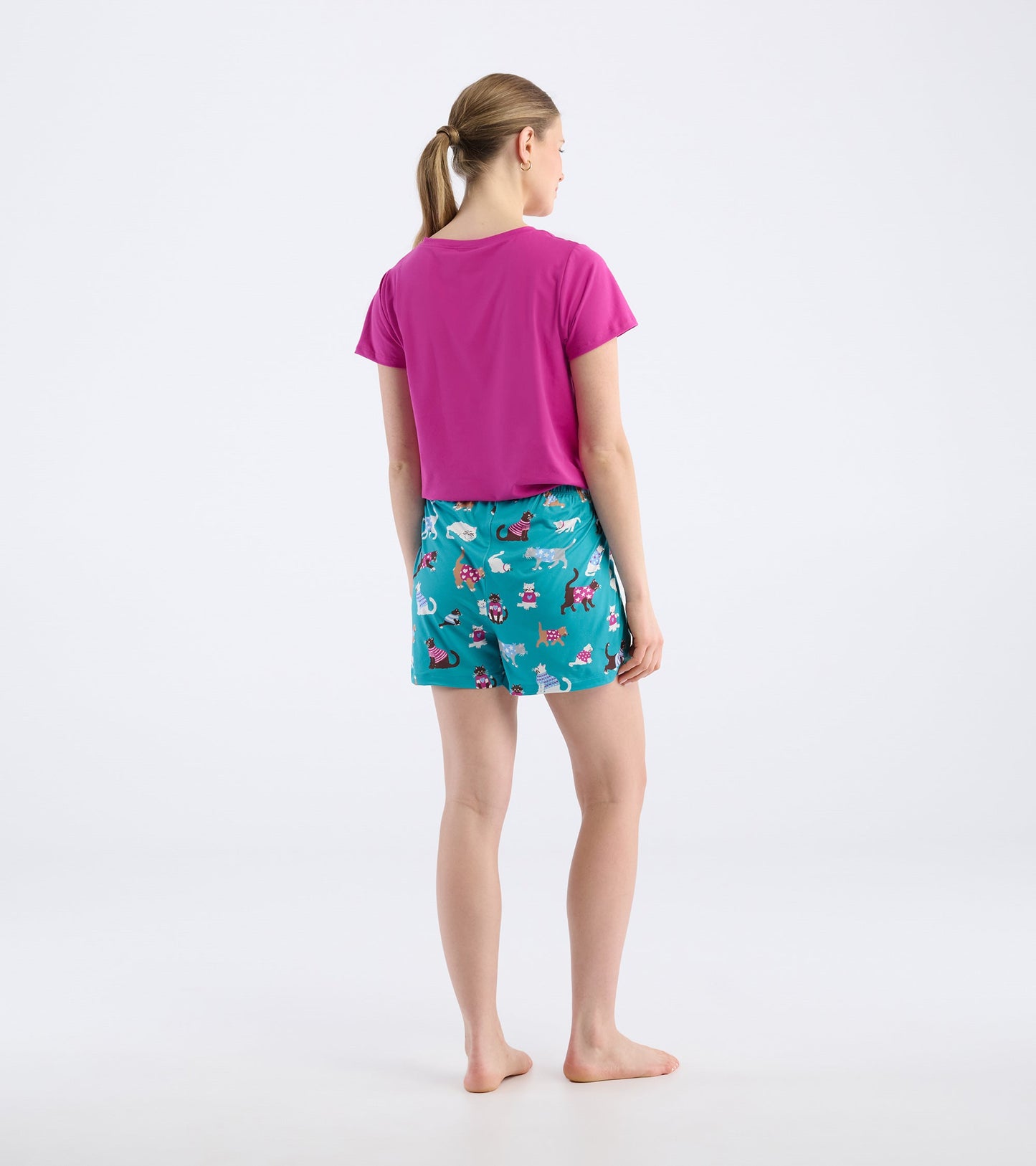 Back view of a woman wearing teal pajama shorts with a cute cat pattern and a pink top.