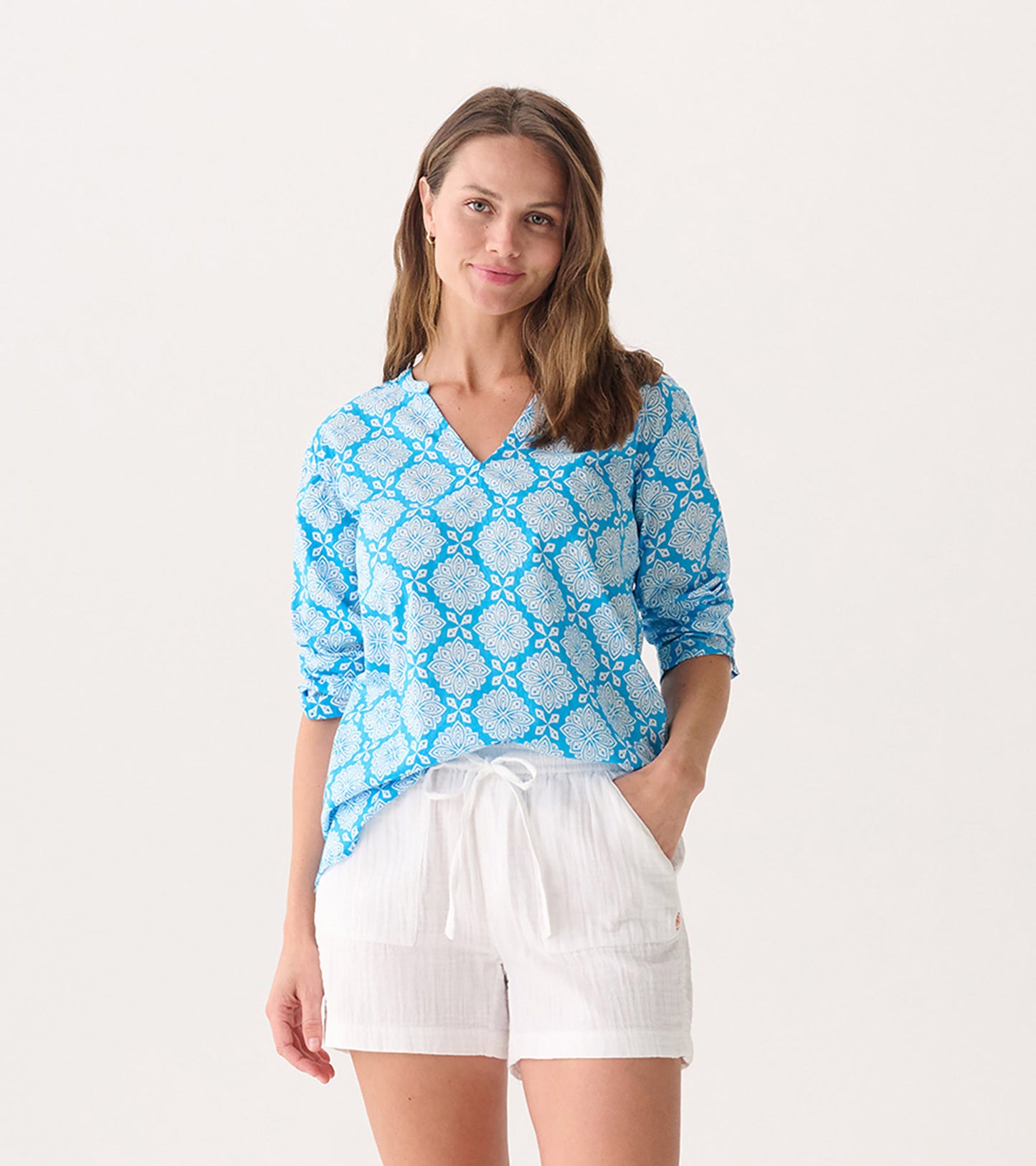 Blue tunic with a white floral pattern, featuring a V-neck and long sleeves, paired with white shorts.