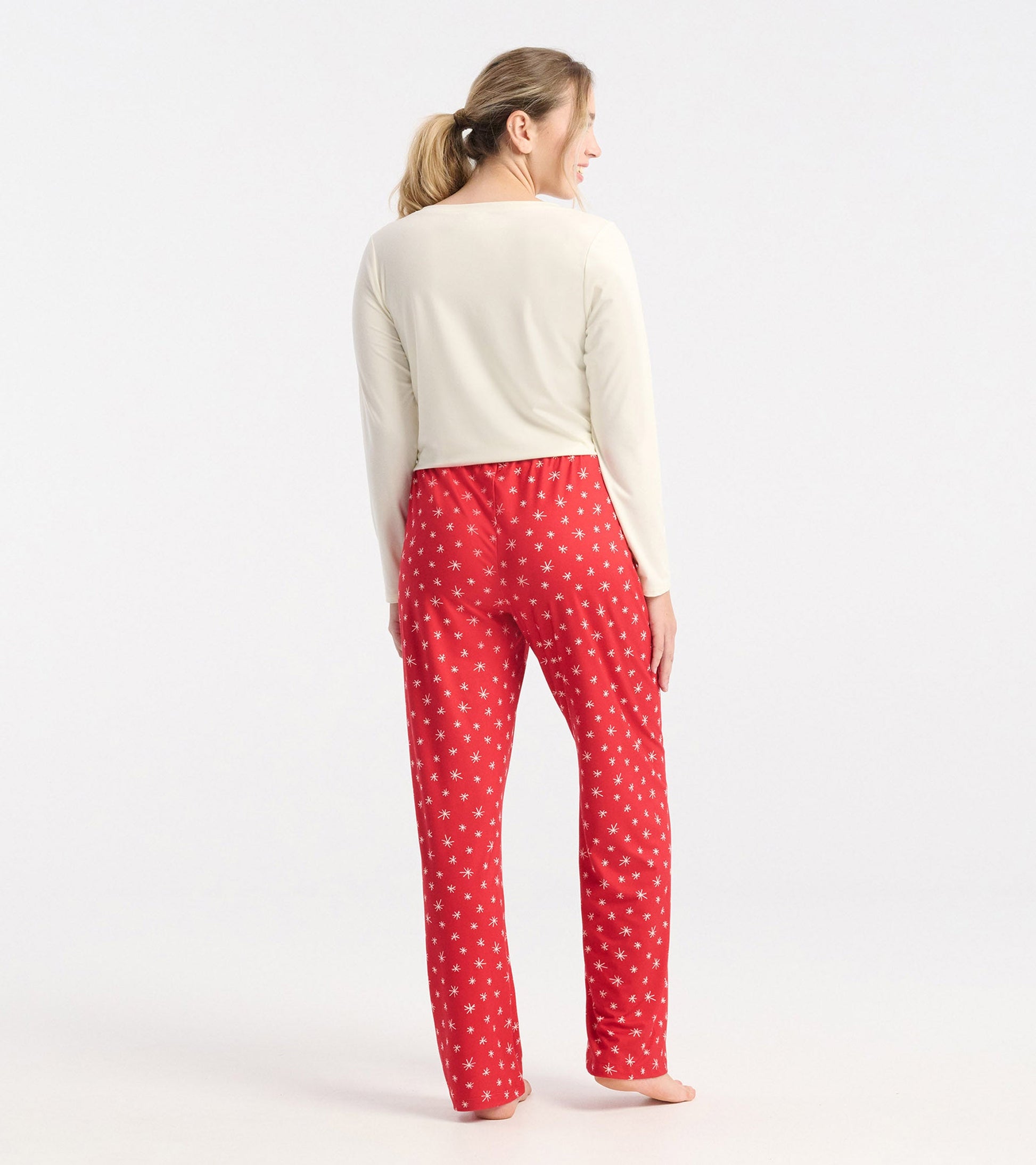 Red polyknit pajama pants with white snowflake pattern, featuring an elastic waistband, shown from the back.