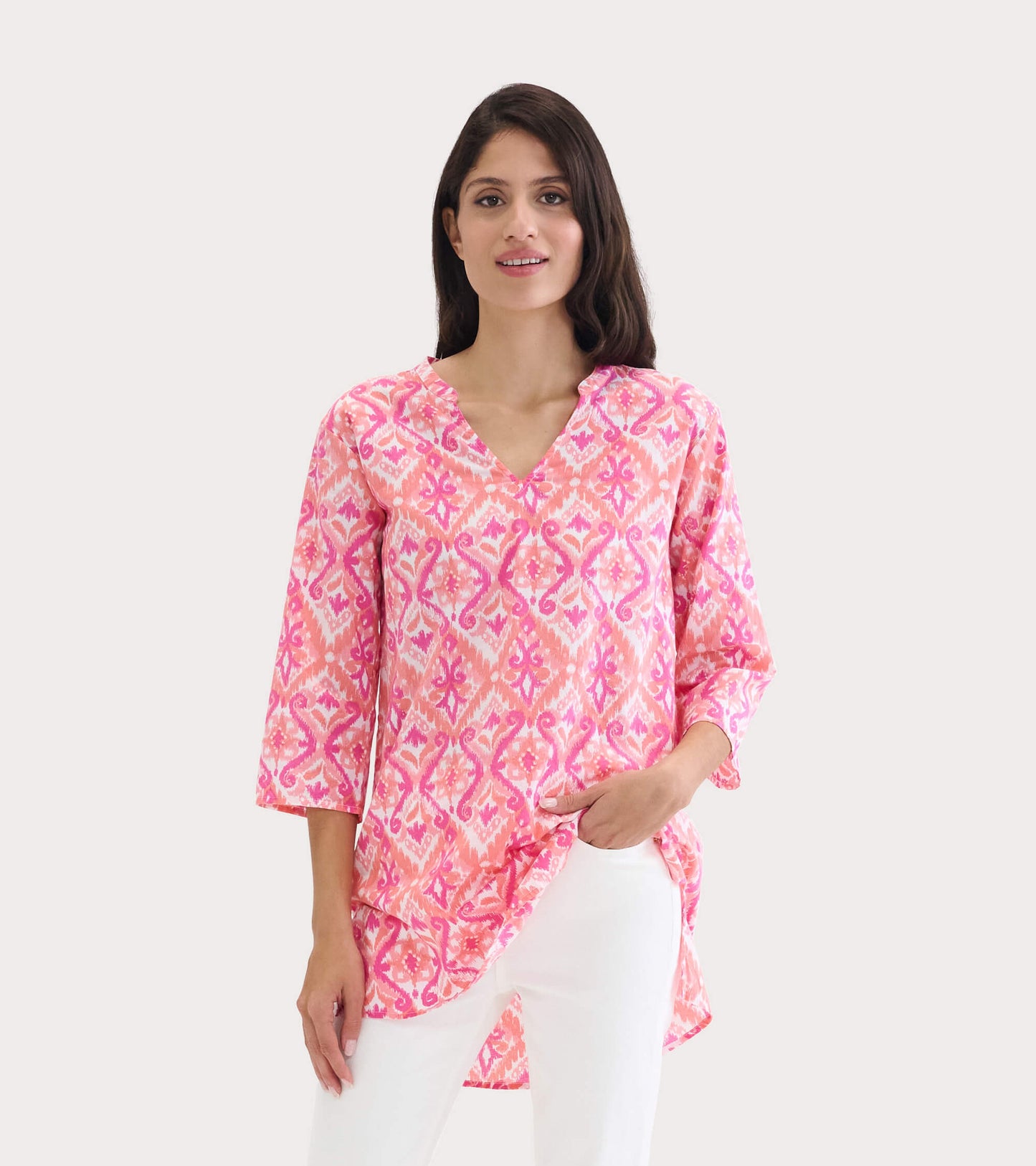 Pink and coral tunic with an ikat pattern, featuring a V-neck and three-quarter sleeves, styled with white pants.