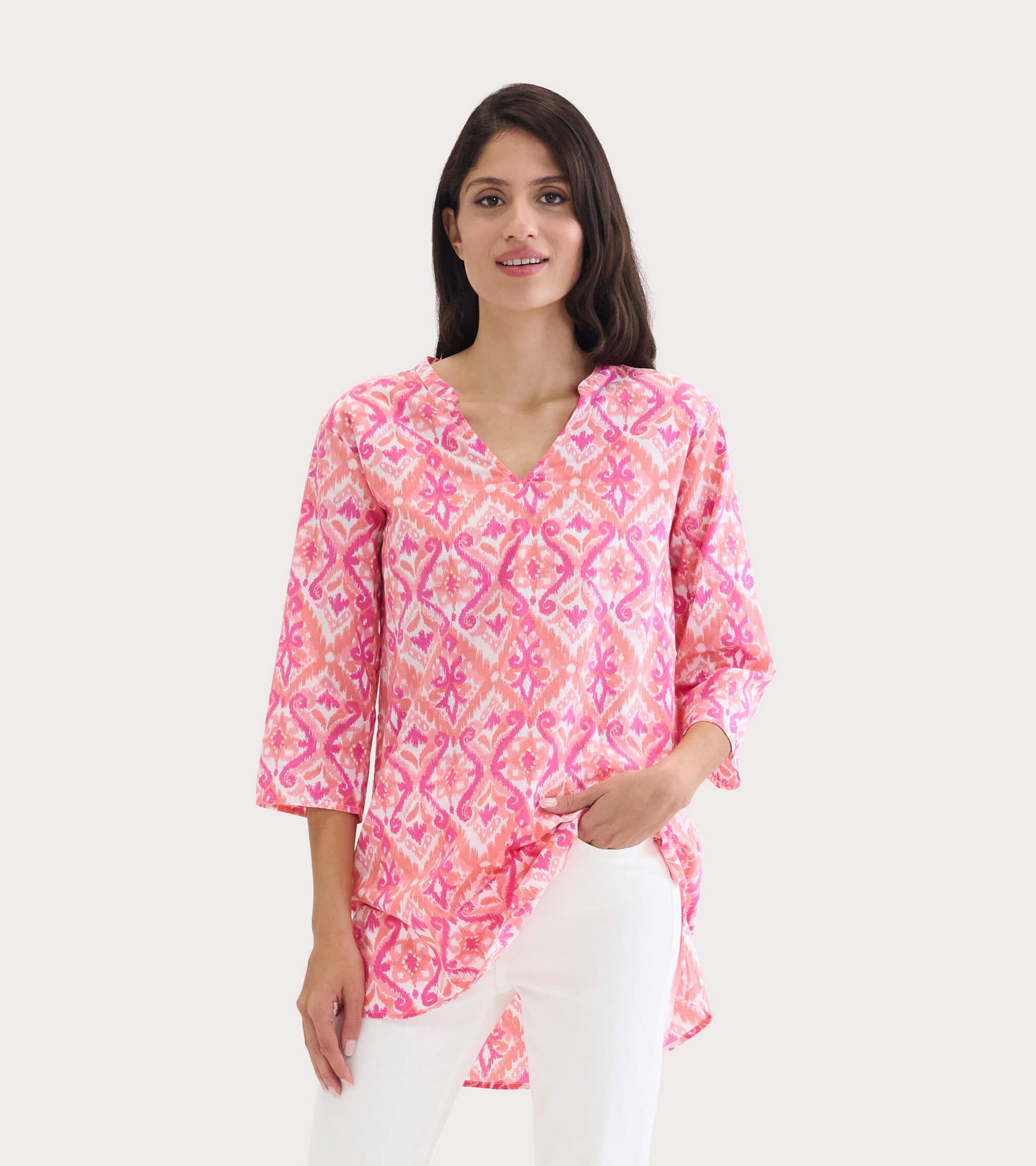 Pink and coral tunic with an ikat pattern, featuring a V-neck and three-quarter sleeves, styled with white pants.