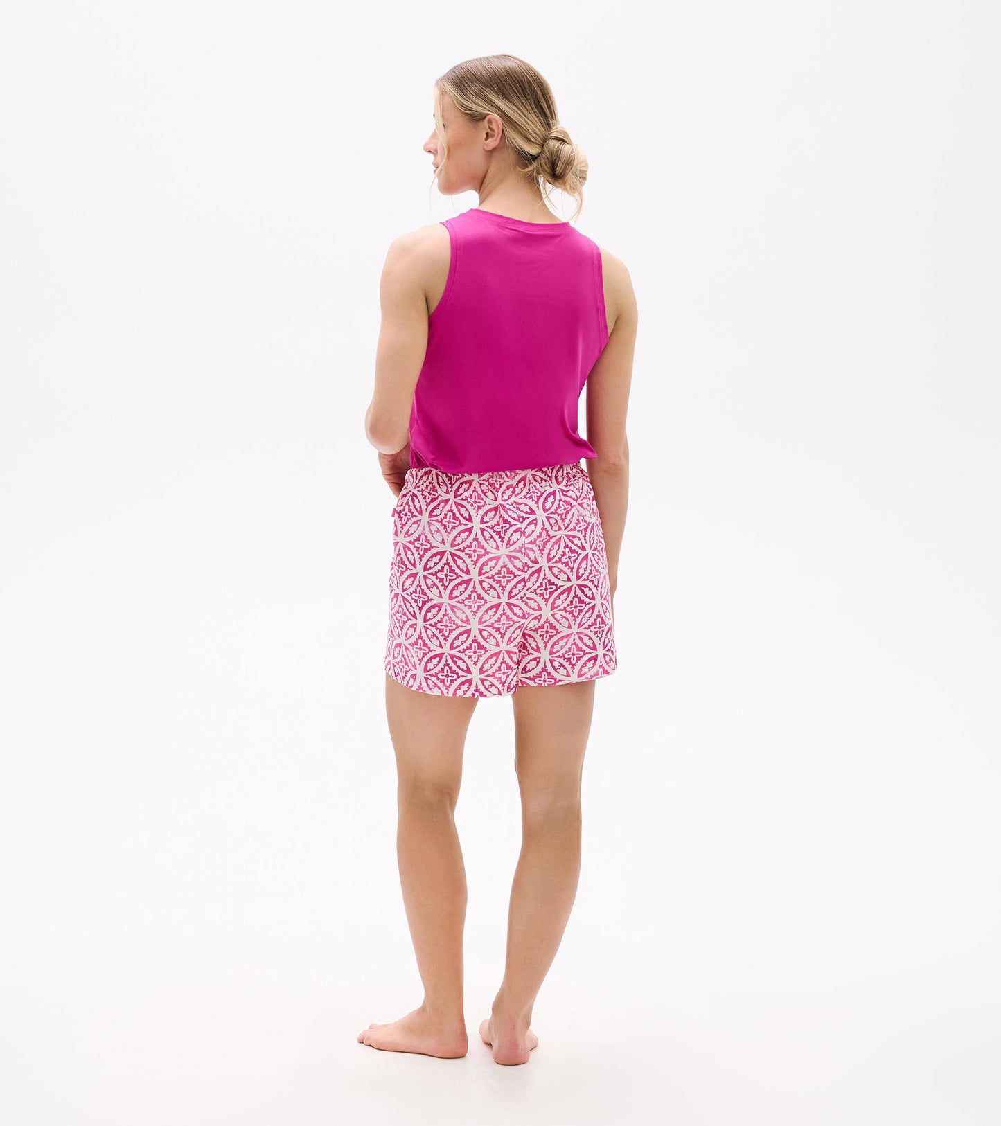 Back view of a woman wearing pink pajama shorts with a floral pattern and a matching pink tank top.