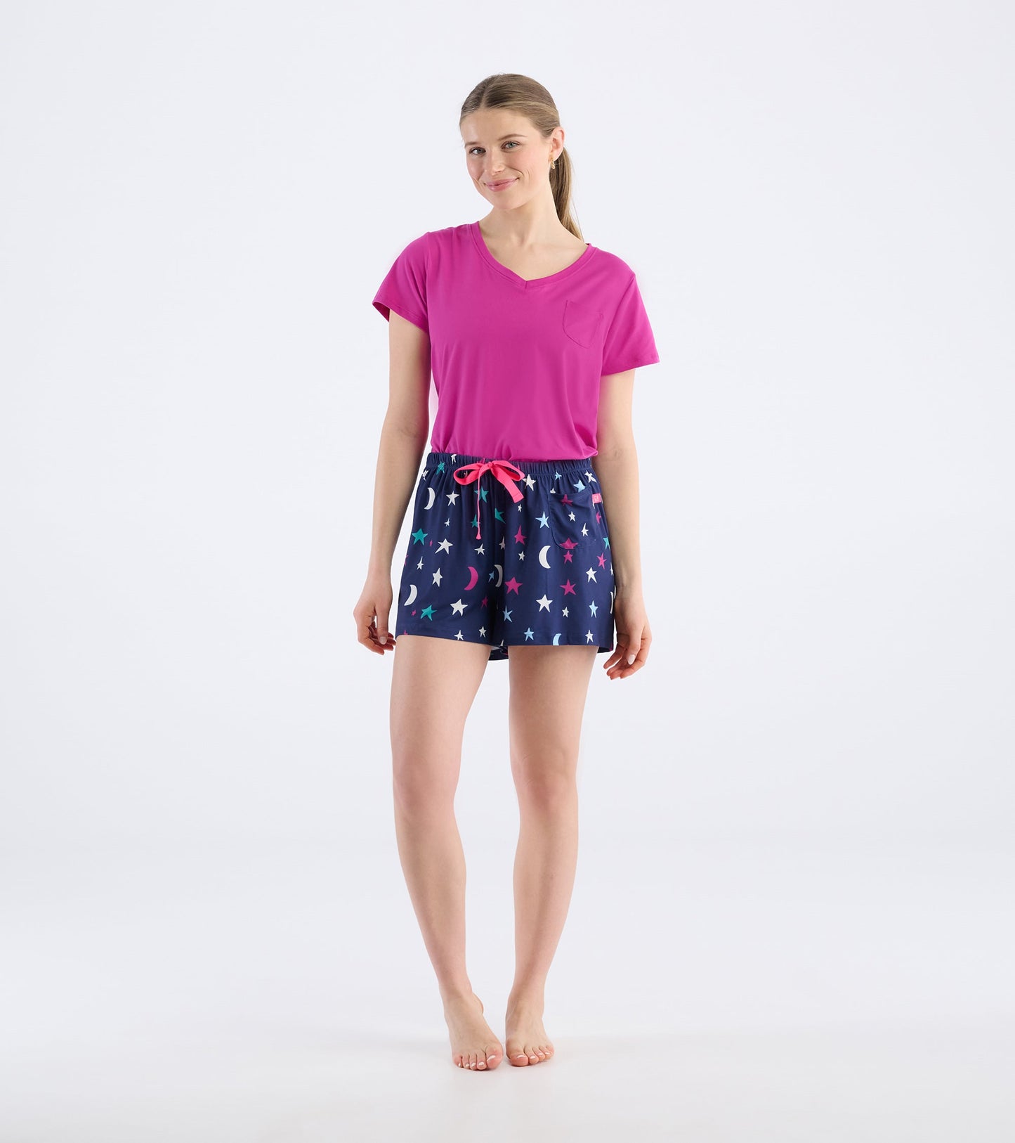 Pink V-neck top paired with navy pajama shorts featuring colorful stars and moons, elastic waistband with a pink drawstring.