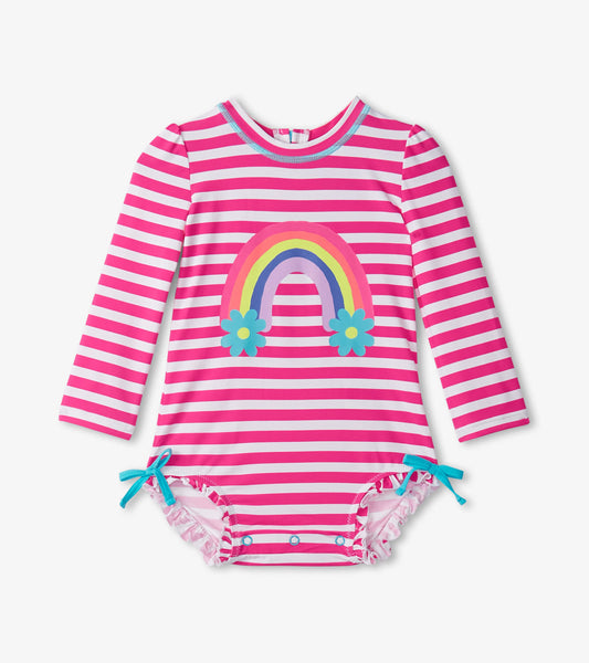 Pink and white striped long-sleeve rashguard swimsuit with rainbow and flower graphic, ruffled edges, and tie details.