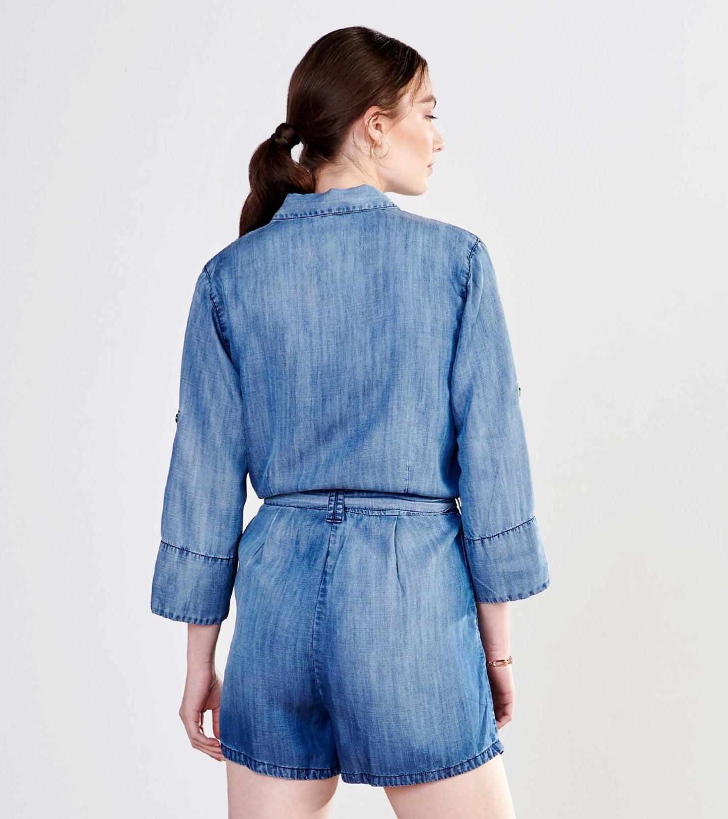 Medium blue wash romper with three-quarter sleeves and a belted waist, shown from the back.