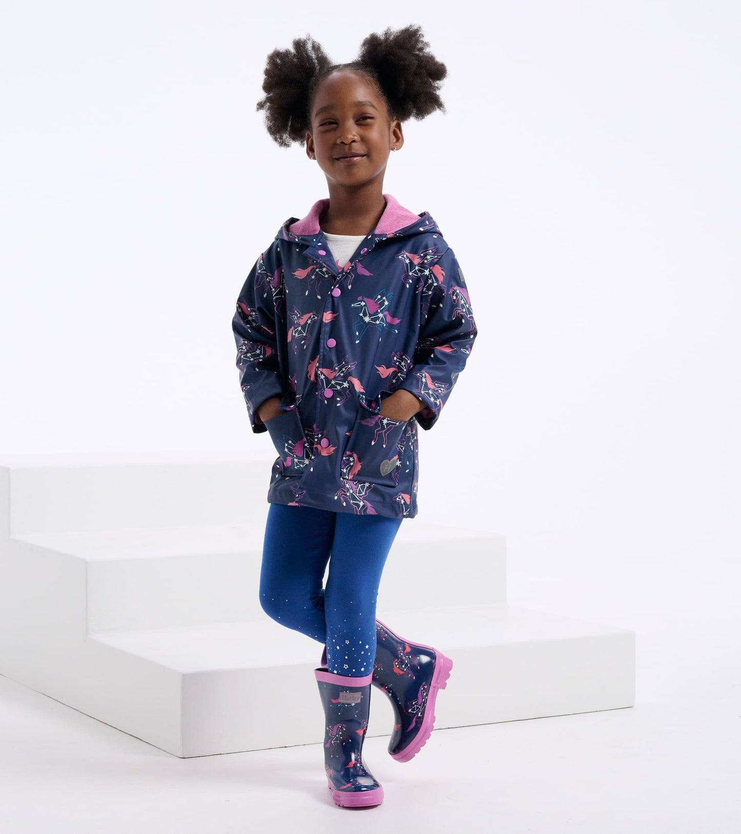 Navy rain jacket with unicorn constellations, pink accents, and pockets, paired with blue leggings and matching rain boots.