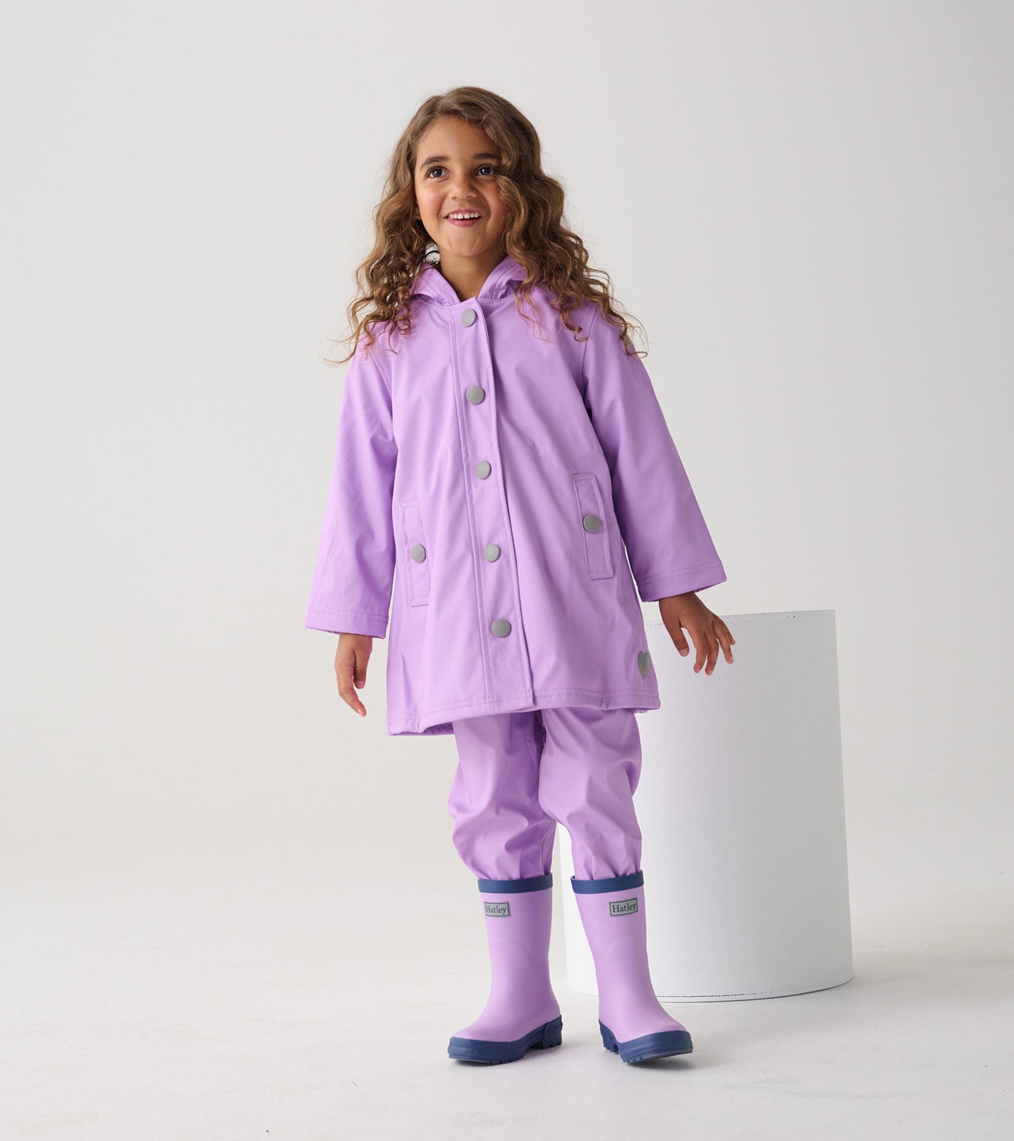 Lilac button-up rain jacket with a hood, featuring silver buttons and side pockets, worn by a smiling girl.