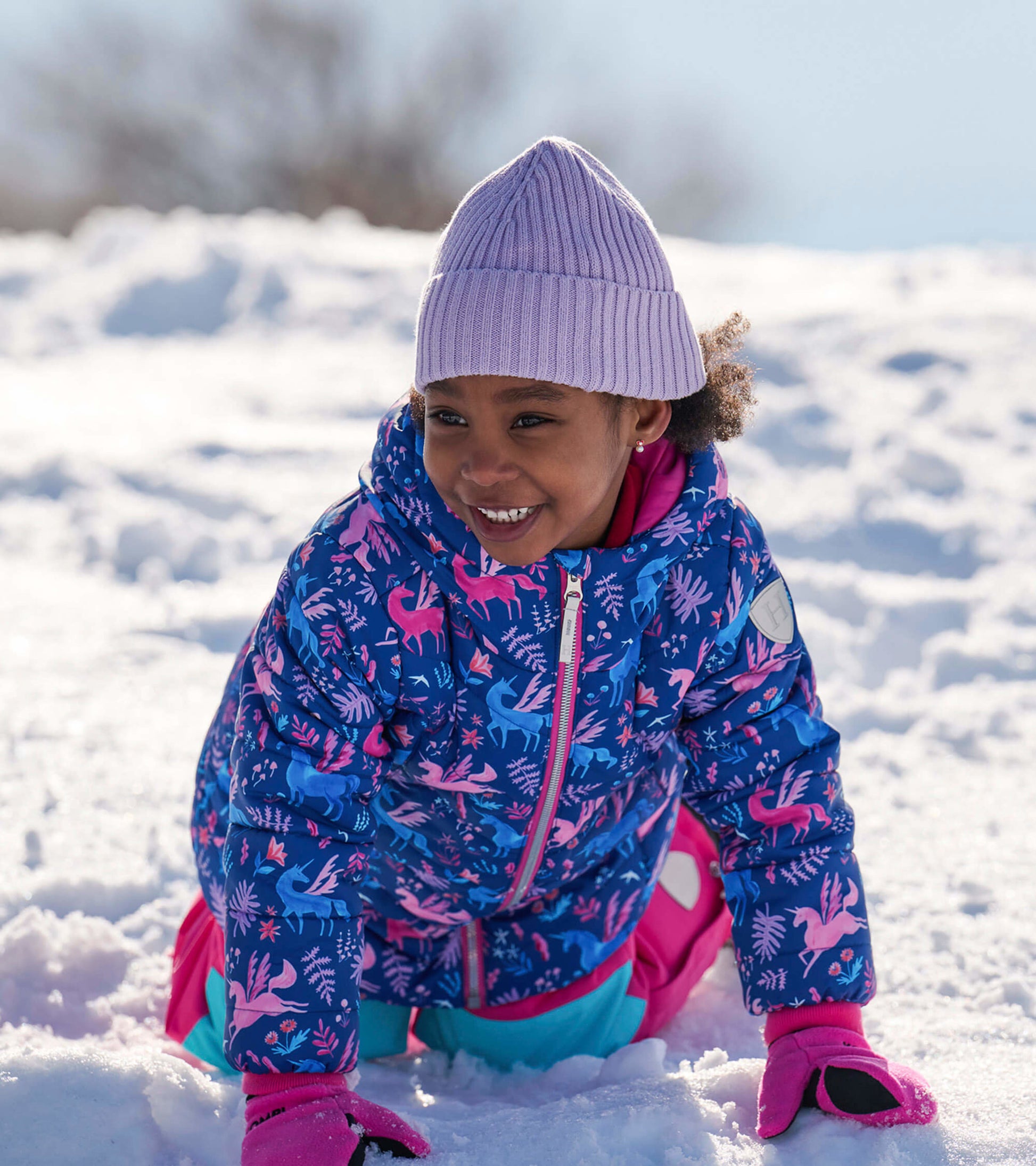Colorful puffer jacket featuring unicorn and floral patterns, worn by a child playing in the snow.
