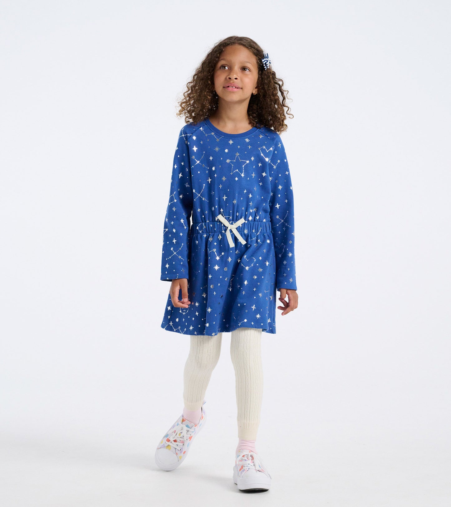 Blue terry dress with constellation print, long sleeves, cinched waist, and a cream tie, paired with cream leggings.