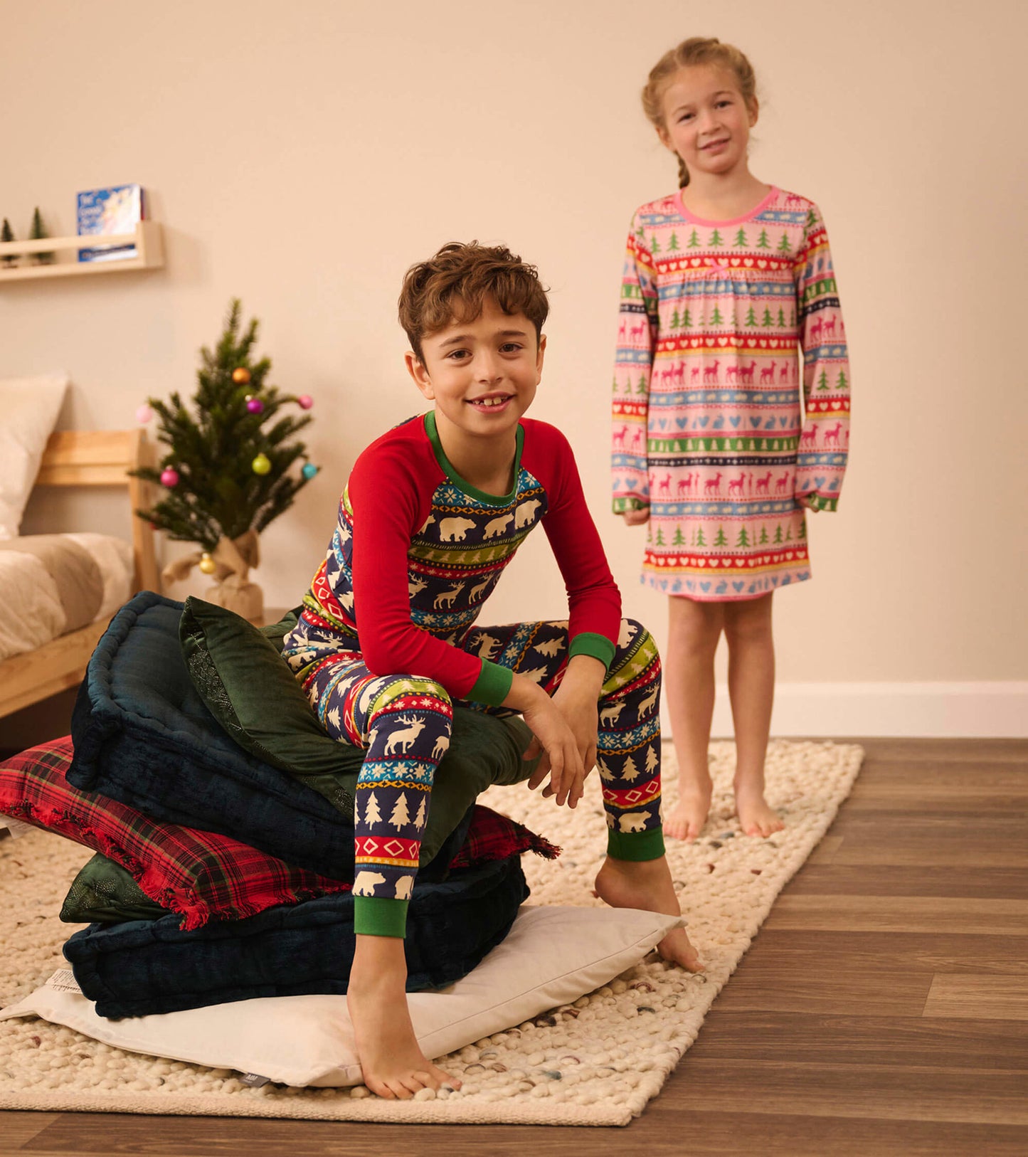 Navy and red Fairisle pajama set for kids, featuring festive patterns, with a boy sitting and a girl standing nearby.