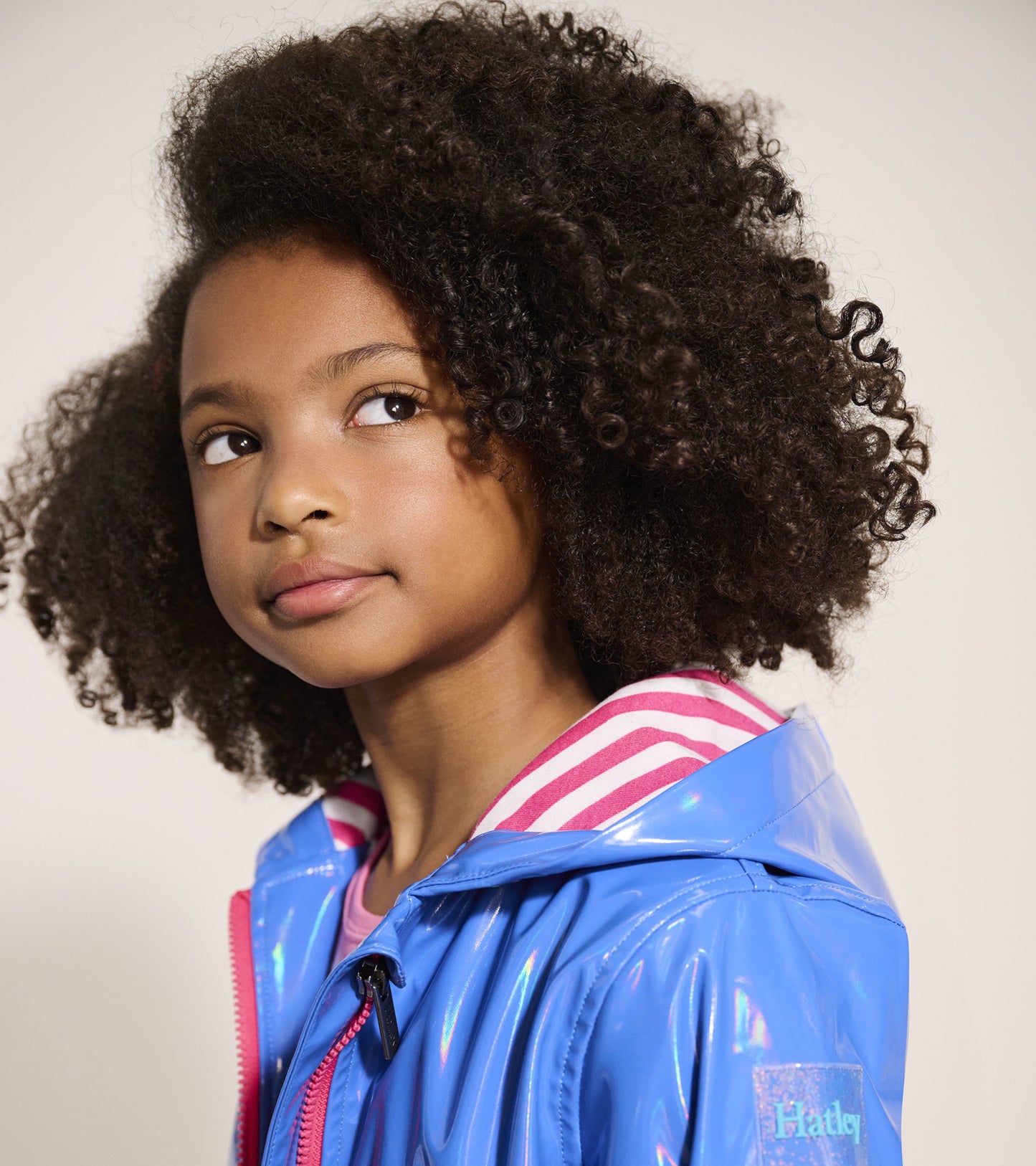 Blue glitter swing jacket with a shiny finish and striped pink hood, designed for girls.