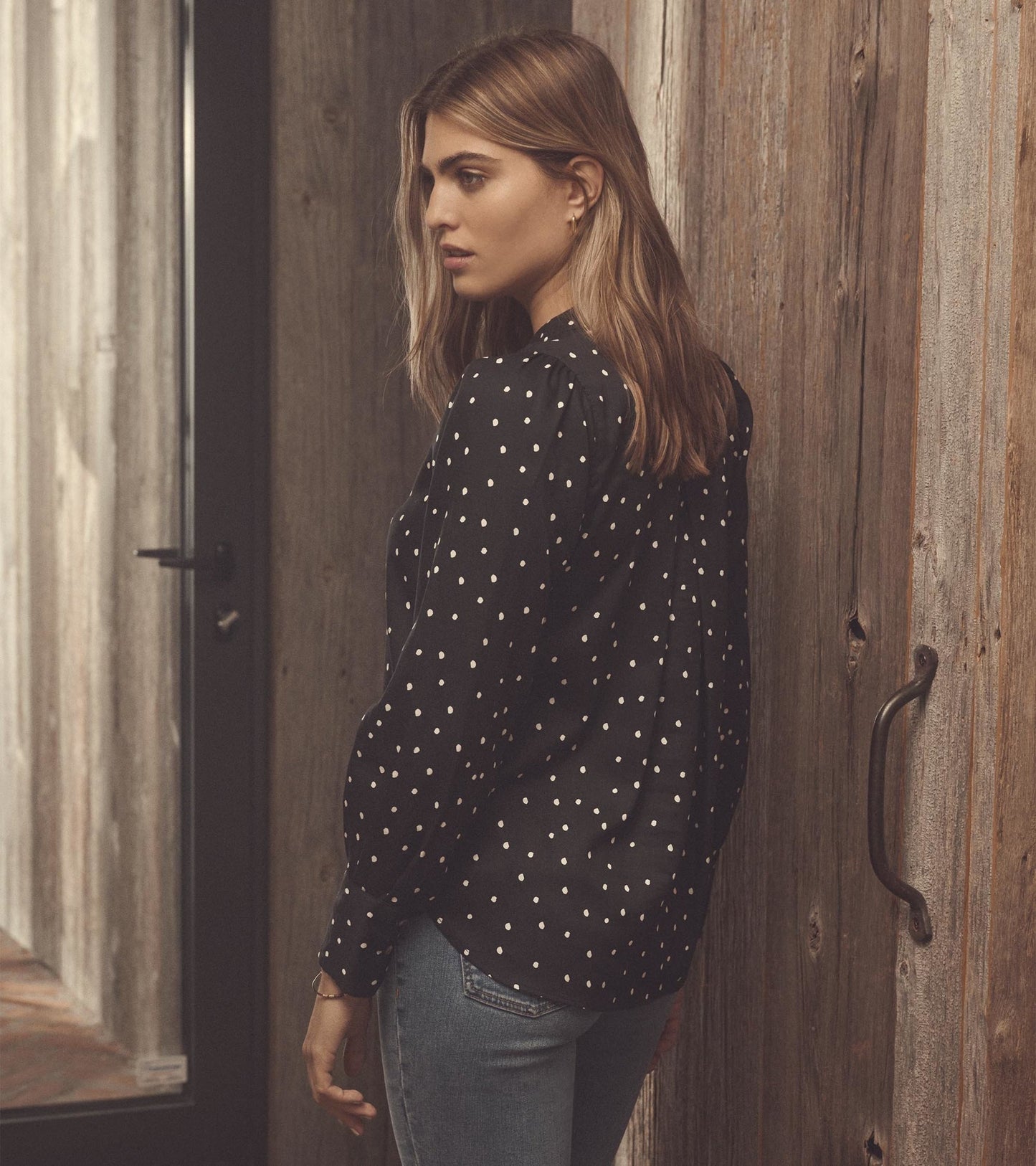 Black blouse with white polka dots, featuring long sleeves and a relaxed fit, styled with blue jeans.