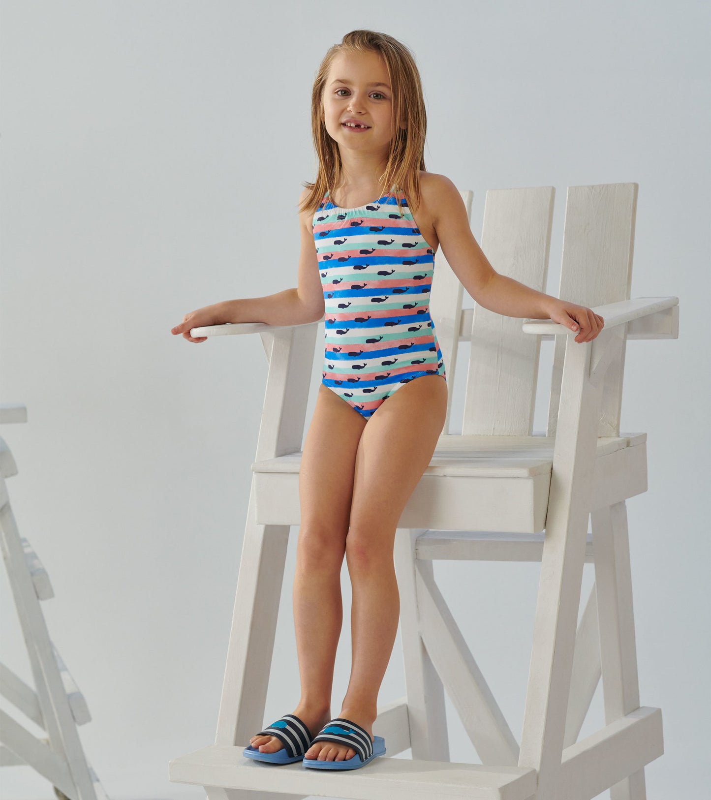 Blue and white striped swimsuit featuring colorful whale patterns, suitable for kids, worn with matching sandals.