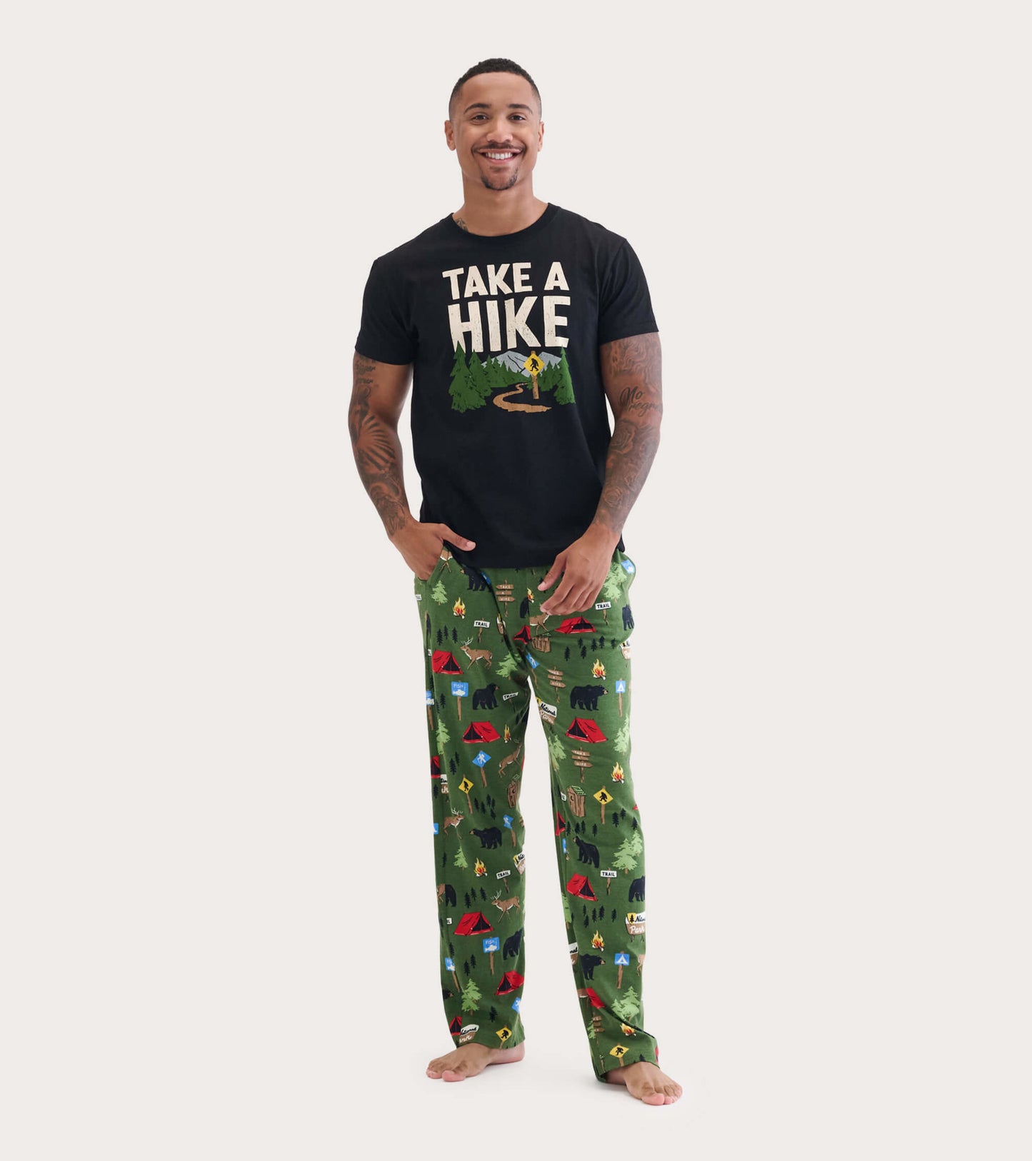 Black short-sleeve tee with "TAKE A HIKE" graphic, paired with green patterned pajama pants featuring camping motifs.