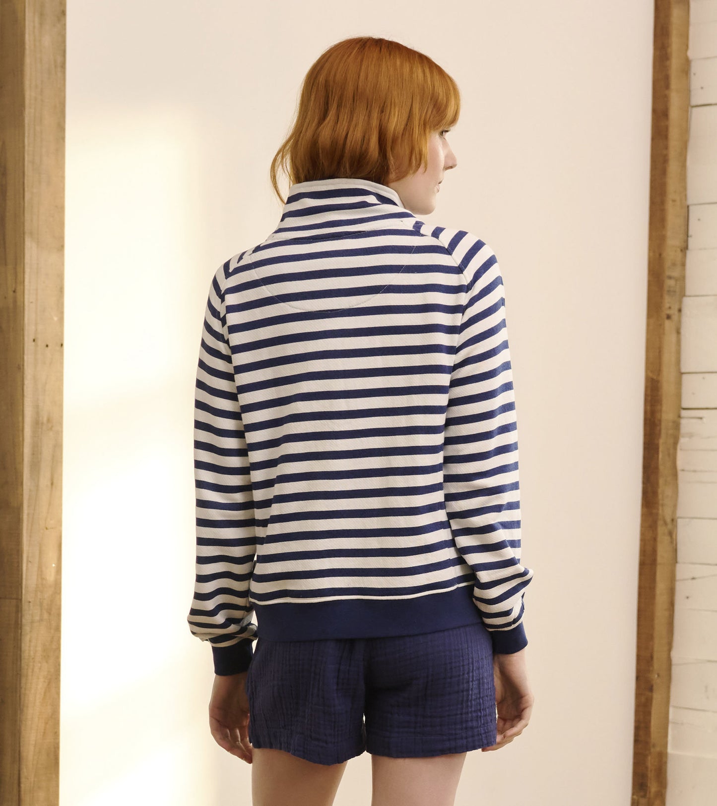 Mock neck pullover in navy and white stripes, featuring long sleeves and a relaxed fit, worn with shorts.