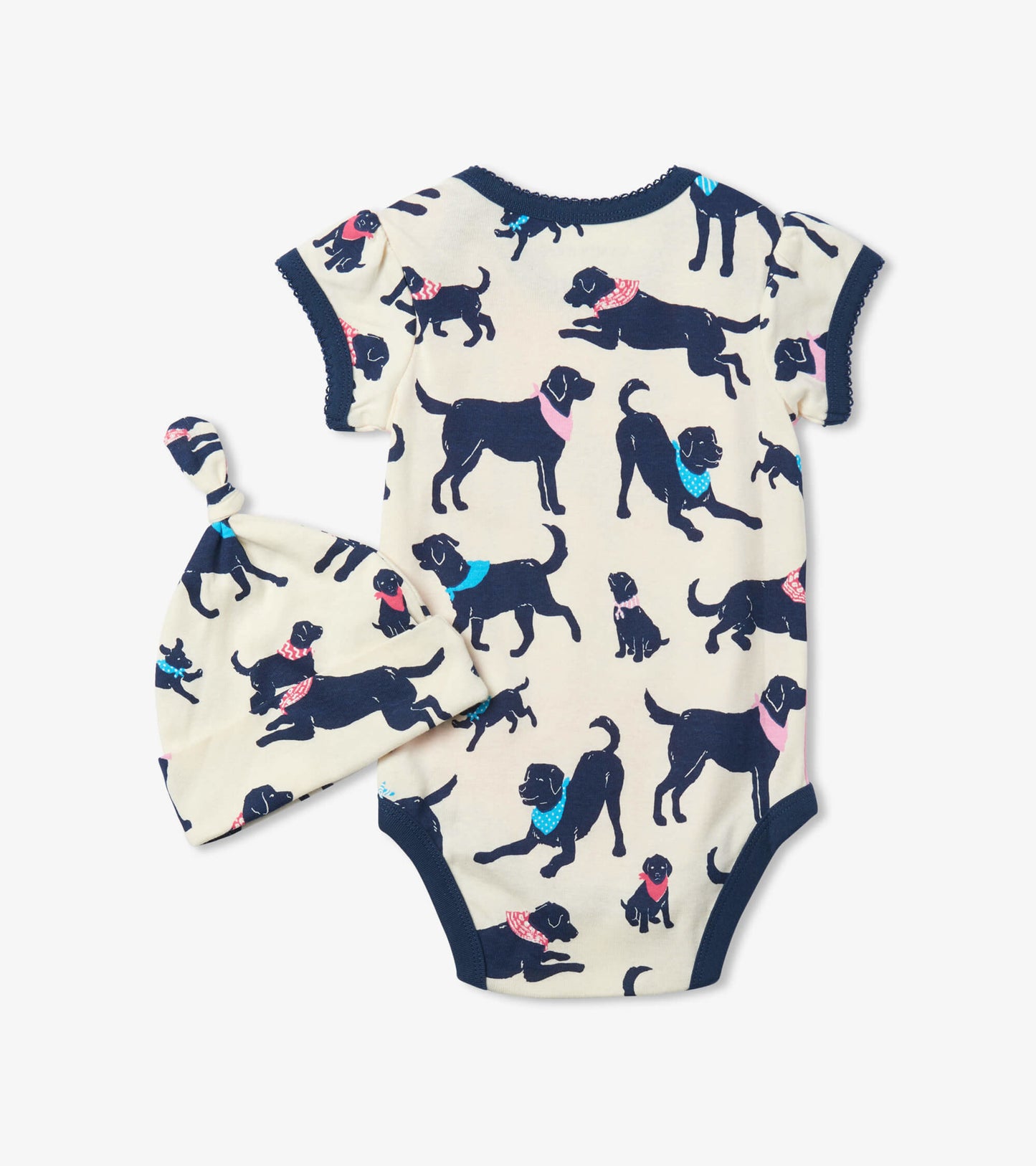 Cream baby bodysuit with playful black dog prints, paired with a matching knotted hat. Short sleeves and soft fabric.