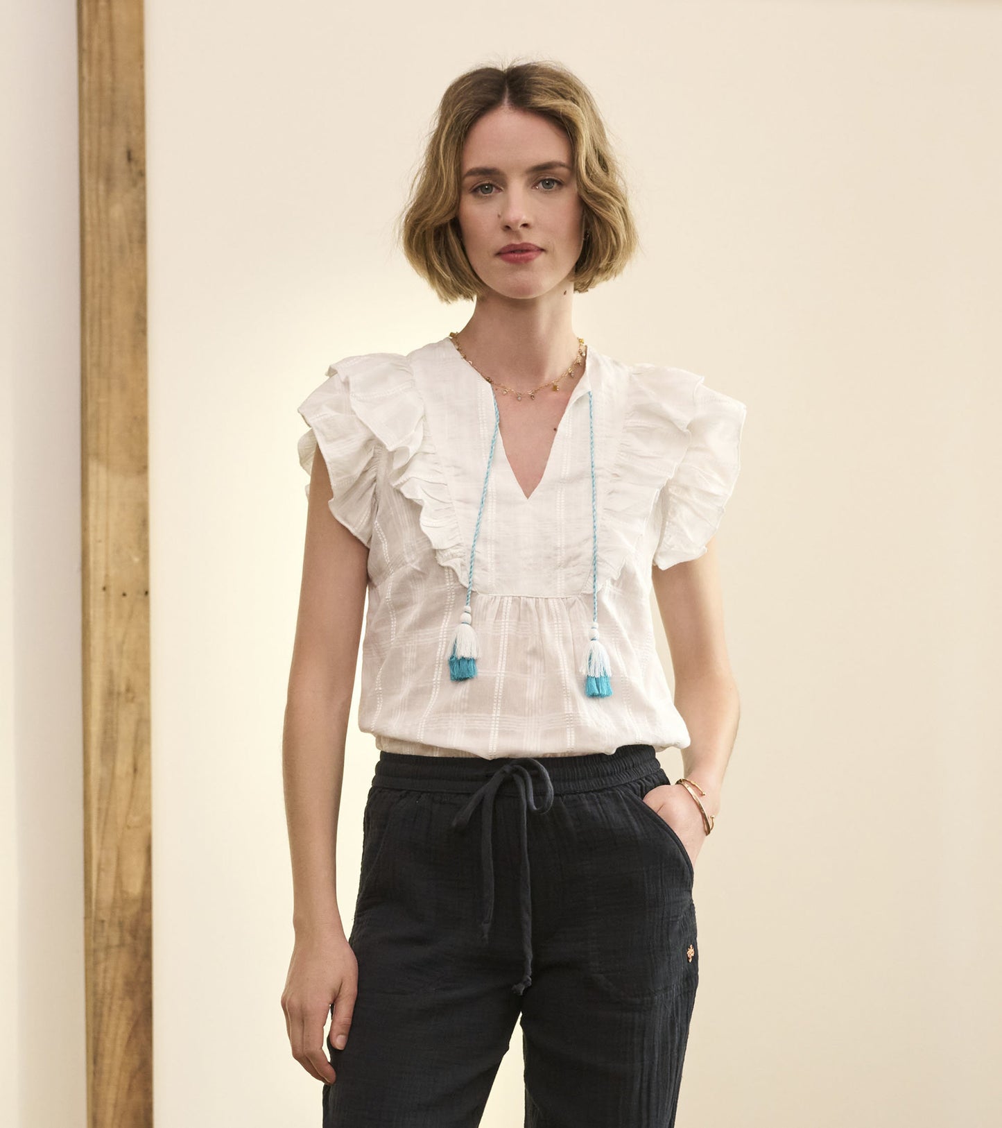 White blouse with ruffled sleeves and a V-neck, paired with dark, relaxed-fit pants.