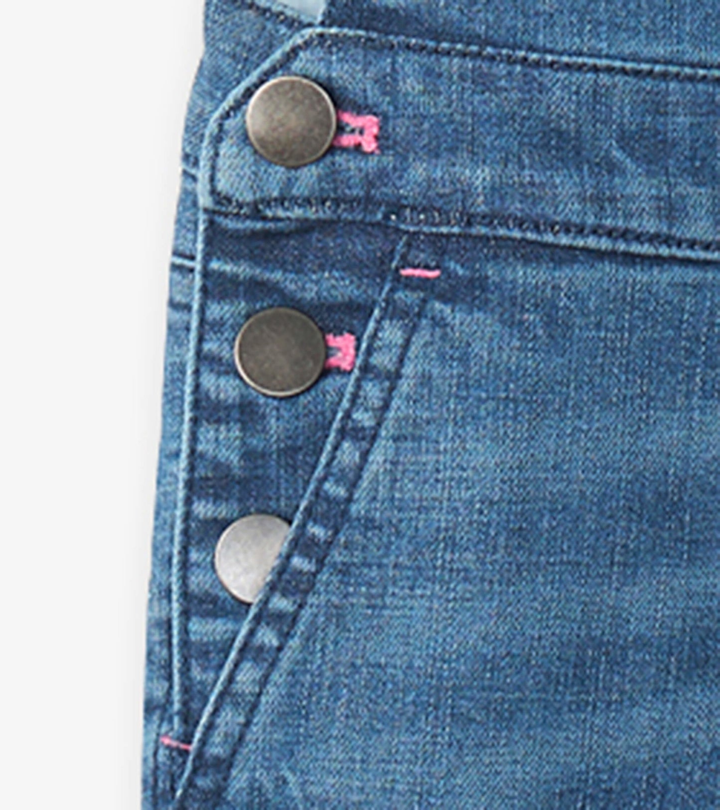 Close-up of blue denim overalls featuring metal buttons and pink stitching details.