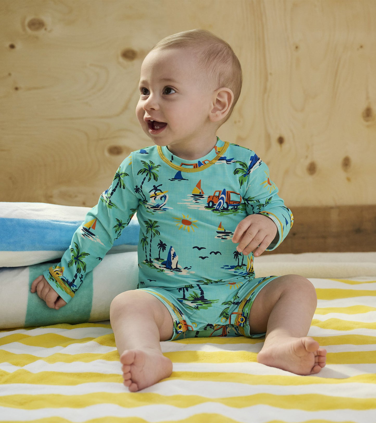 Light blue long-sleeve rashguard with a tropical print, featuring boats and palm trees, worn by a smiling baby boy.