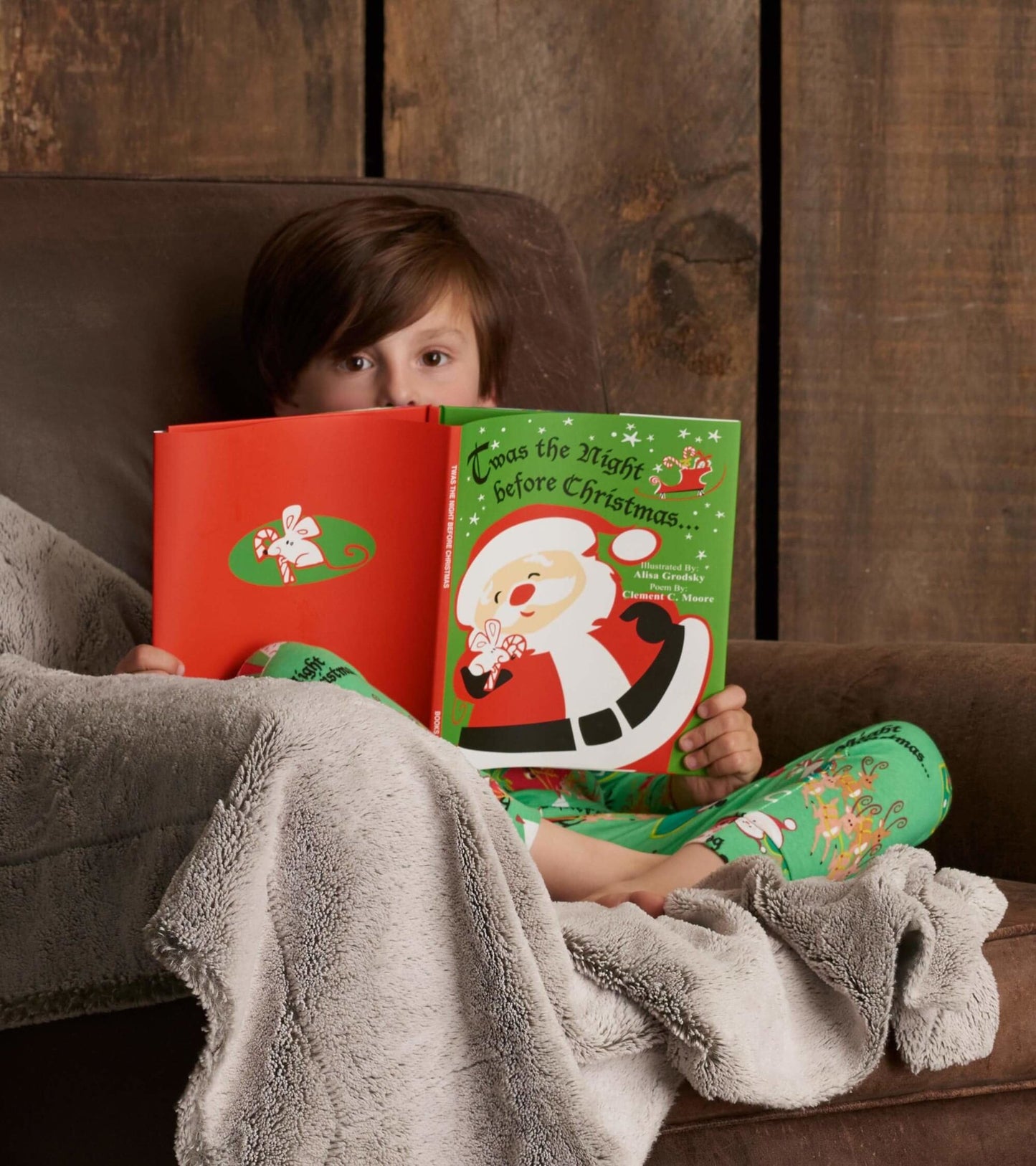 Green pajama set with festive Christmas patterns, worn by a child reading a holiday book while seated on a couch.