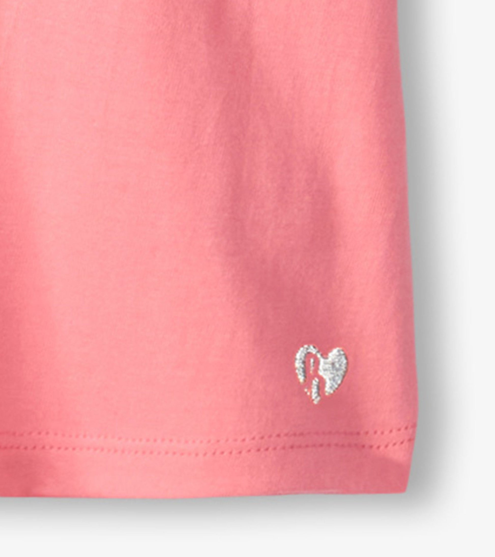 Pink short-sleeve tee with twisted sleeves and a small silver heart logo at the hem. Soft cotton material.