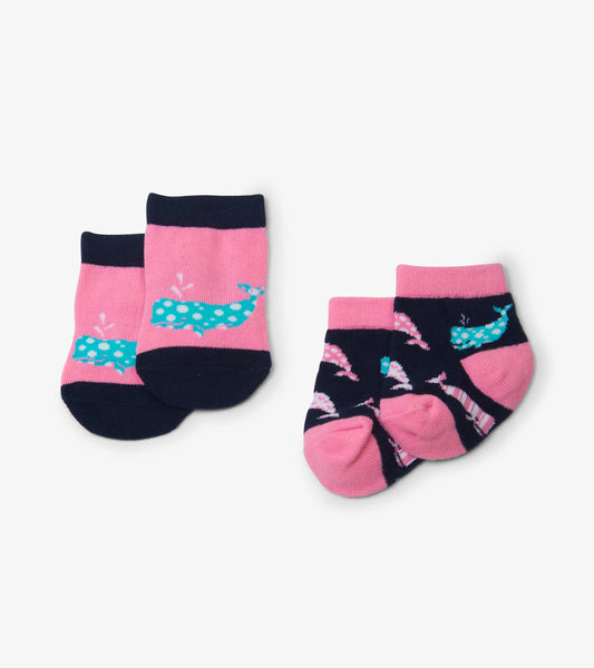 Pink baby socks featuring whale designs, one pair with solid pink and blue whales, the other with patterned whales on navy.