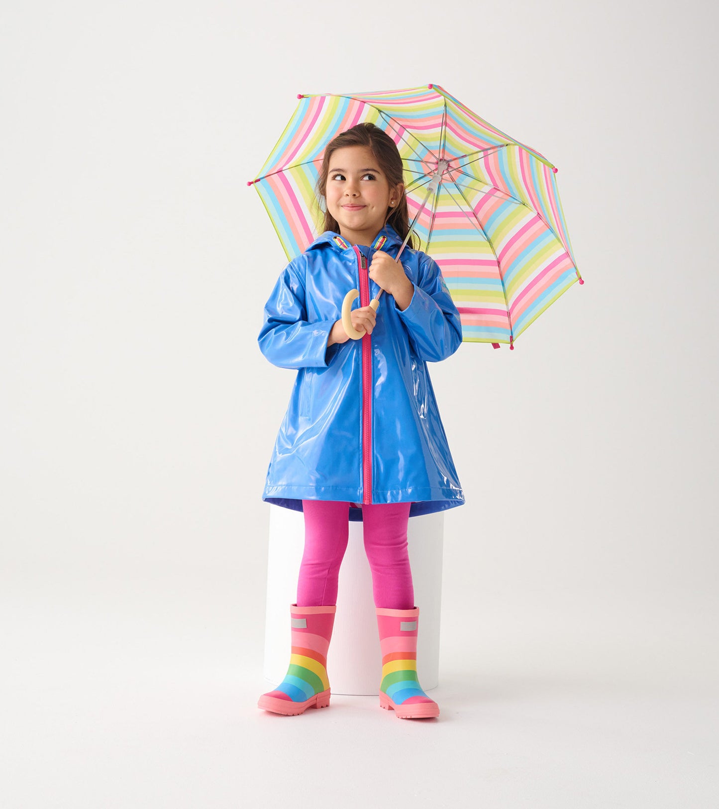 Blue glitter swing jacket with a hood, worn by a girl holding a colorful striped umbrella, paired with pink leggings and rai…